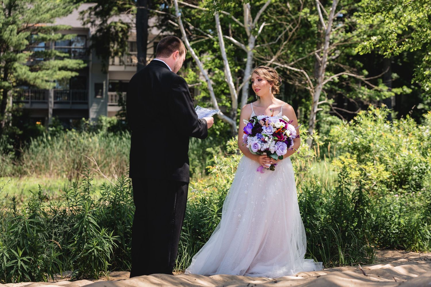 A couple in wedding attire sits together on a stone bench in a lush garden setting during their special day.