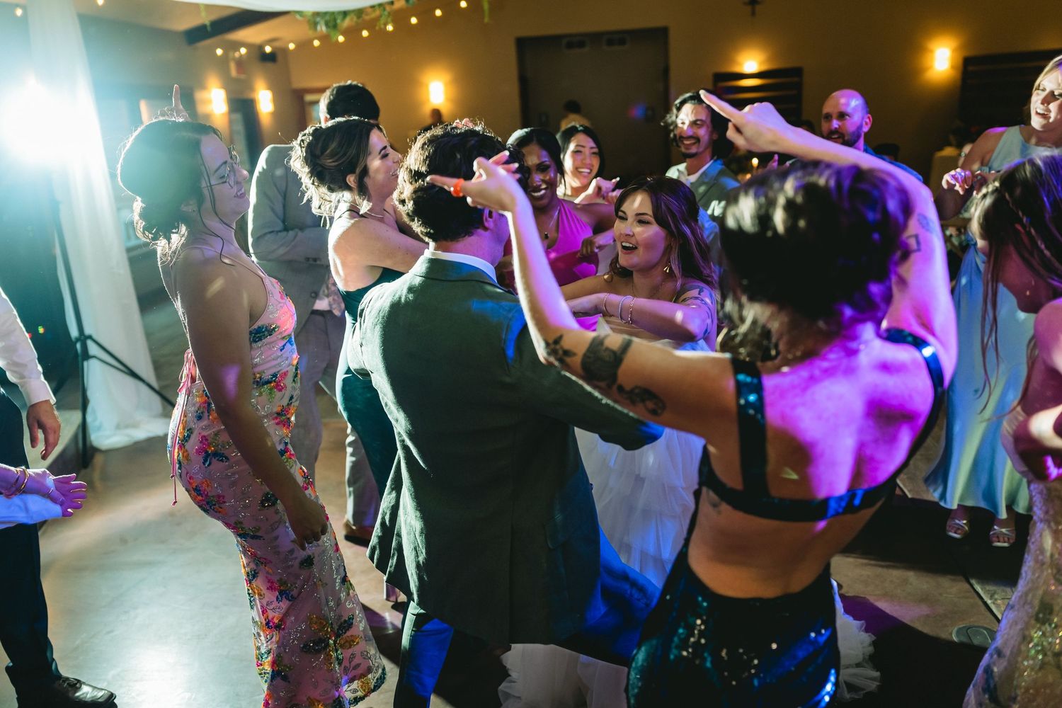 Guests dancing energetically at a lively wedding reception with colorful purple lighting and festive atmosphere.
