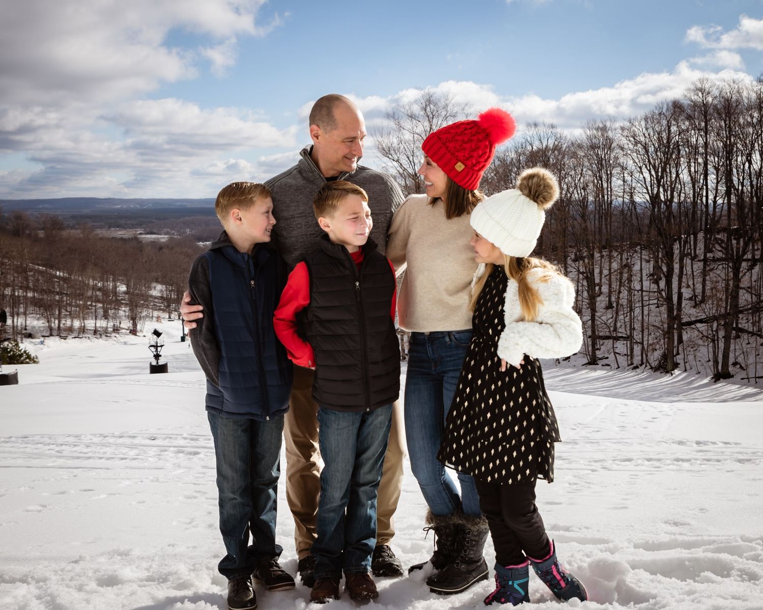 Family of five posing together in snowy winter landscape, children wearing colorful hats and coats, hills of Crystal Mountain in background.