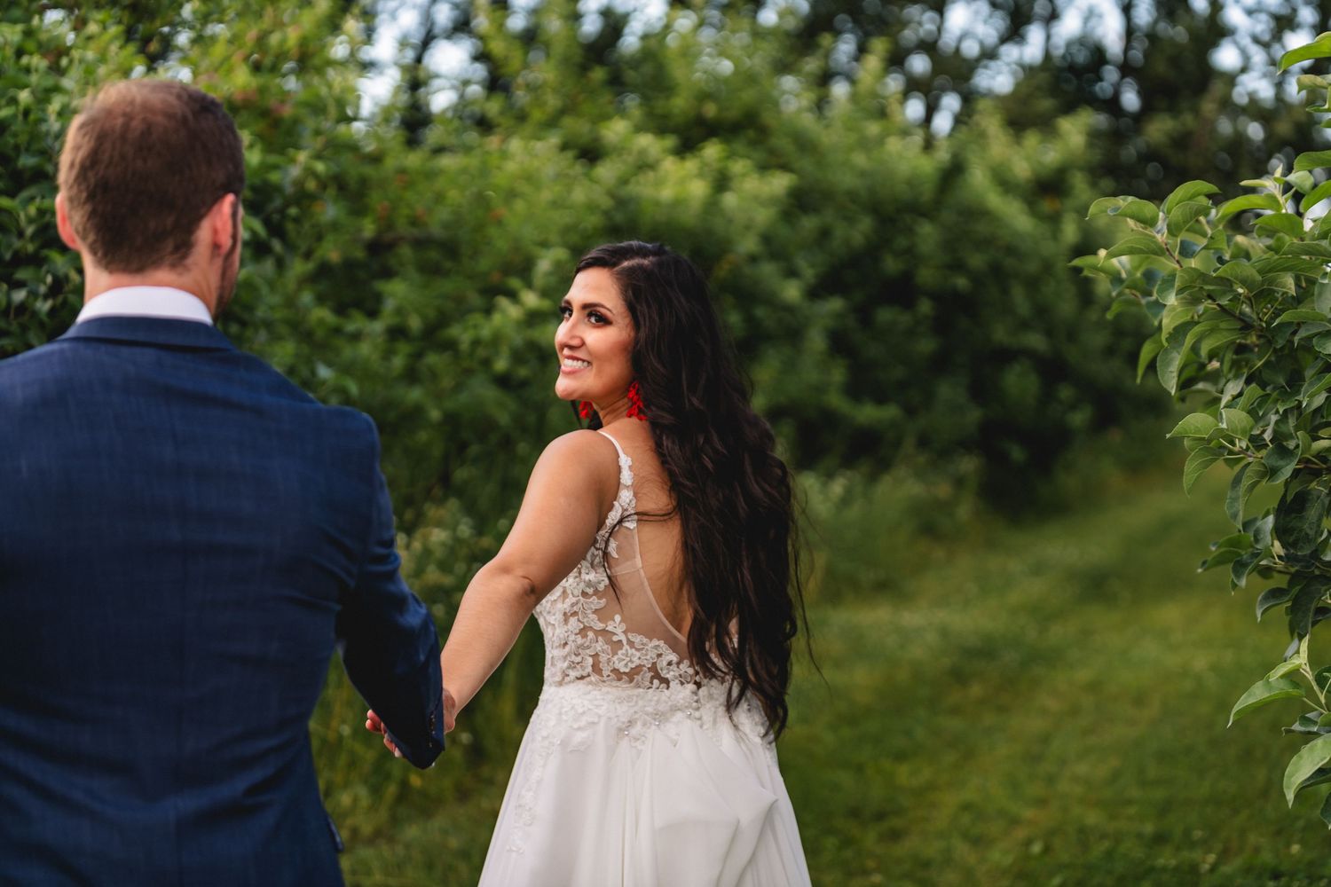A couple in wedding attire embraces while standing in a lush green garden setting.