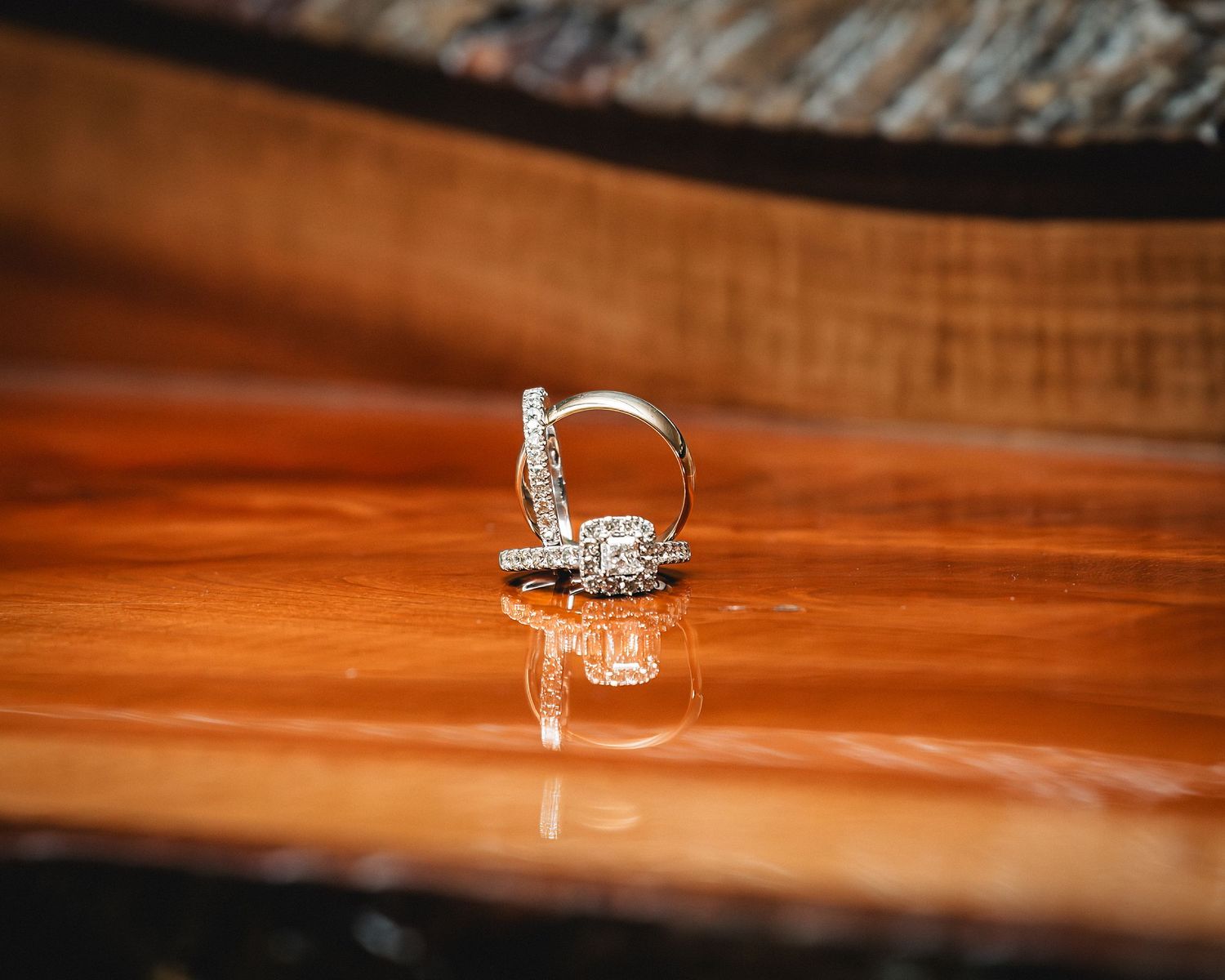 Diamond engagement ring and wedding band displayed on a polished wooden surface with elegant reflection.