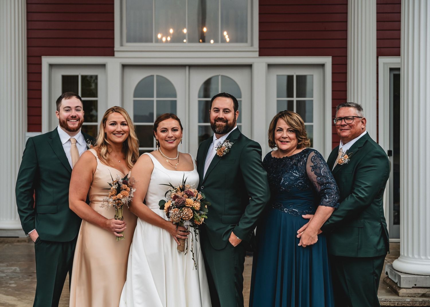 Wedding party members in dark green suits and champagne dresses pose together for formal group photos.