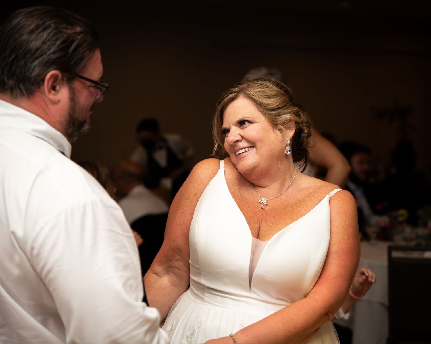 Bride in white wedding gown smiling joyfully while dancing with groom at elegant wedding reception.