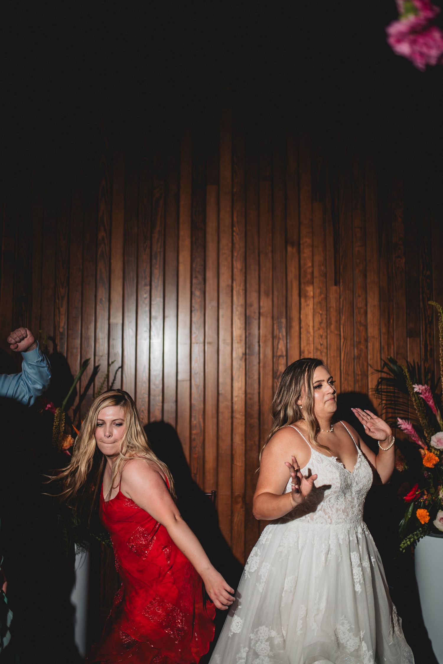 Wedding party dancing and celebrating on the dance floor with wooden paneled walls in a dark reception venue.