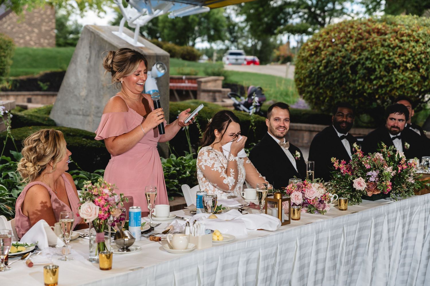 Wedding guests enjoy an elegant outdoor reception dinner at long tables decorated with floral centerpieces.