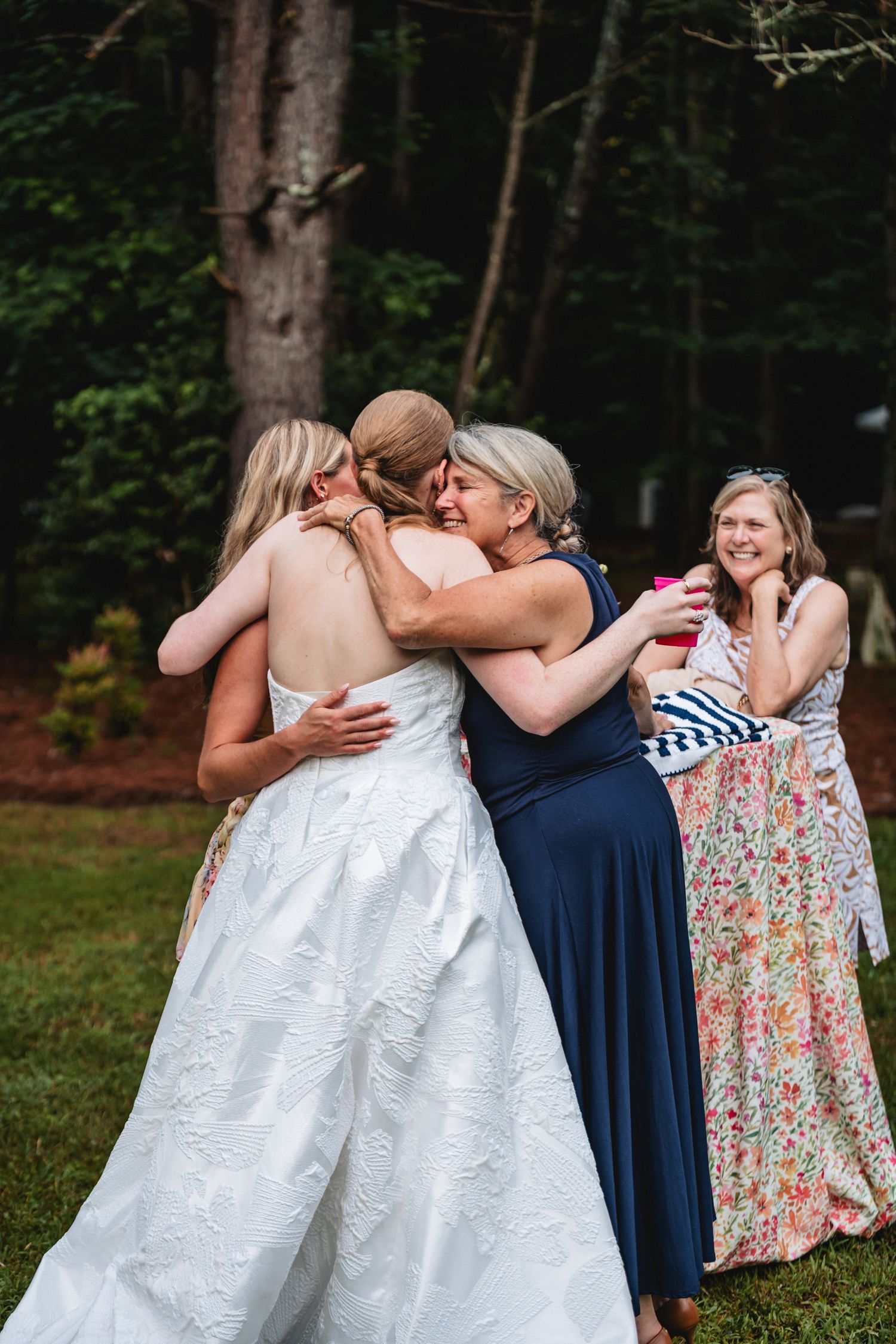 Two people in wedding attire share a tender kiss while others look on during an outdoor celebration.