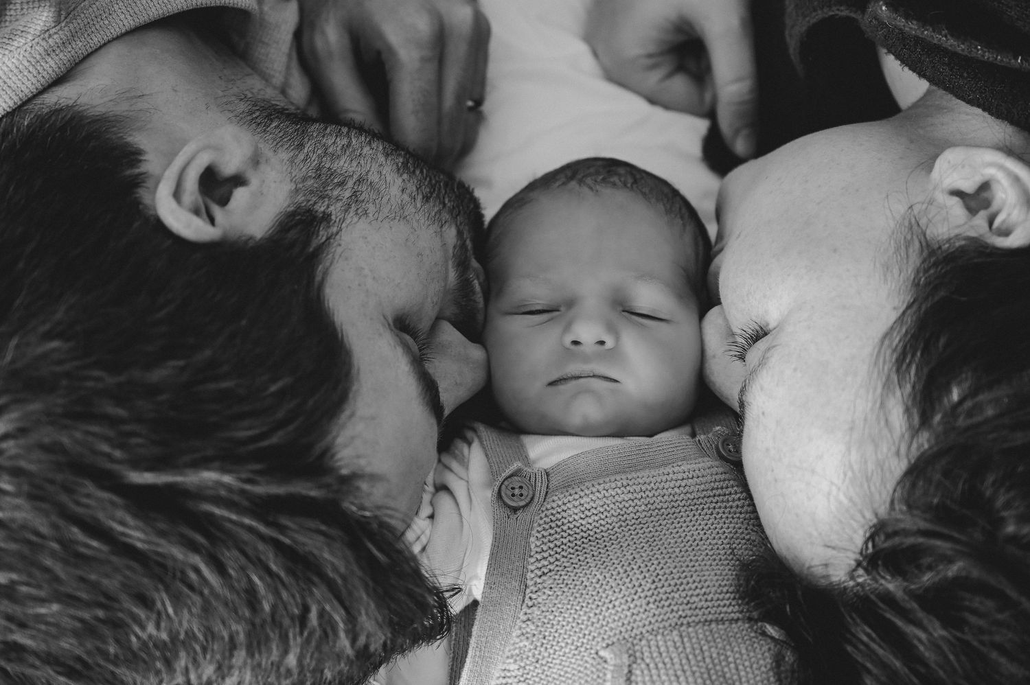 Mom and Dad laying with newborn baby boy kissing him on the cheek in their Westminster, Colorado newborn lifestyle session