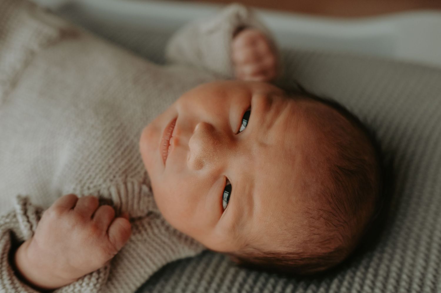 Close-up portrait of a peaceful newborn baby lying on a soft green knit blanket wearing a beige onesie.