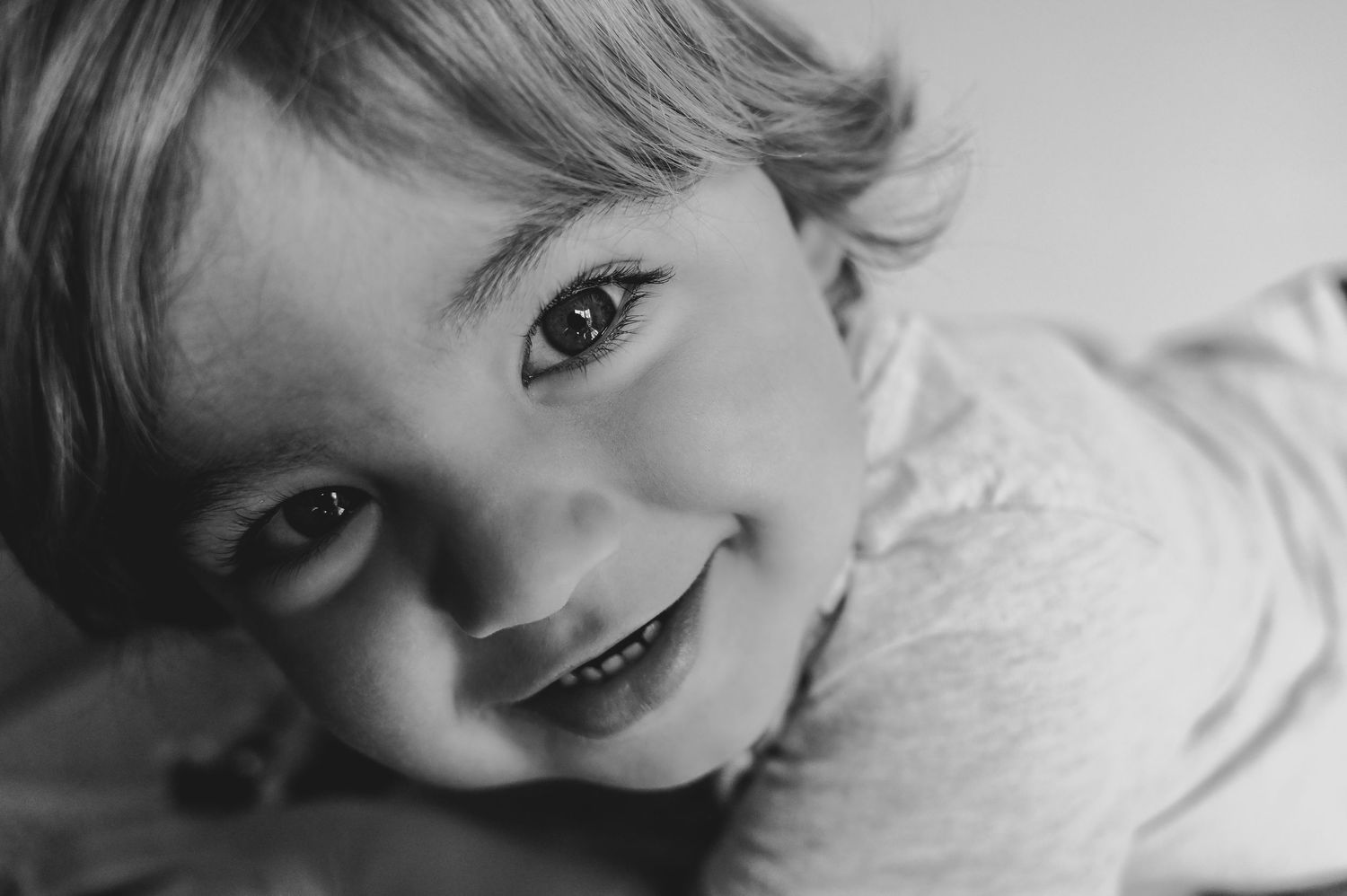 Close-up black and white portrait of a smiling young child with bright eyes and curly hair.