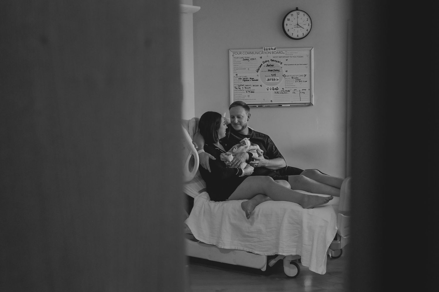 Black and white photo of couple in hospital bed tenderly holding their newborn baby after birth.