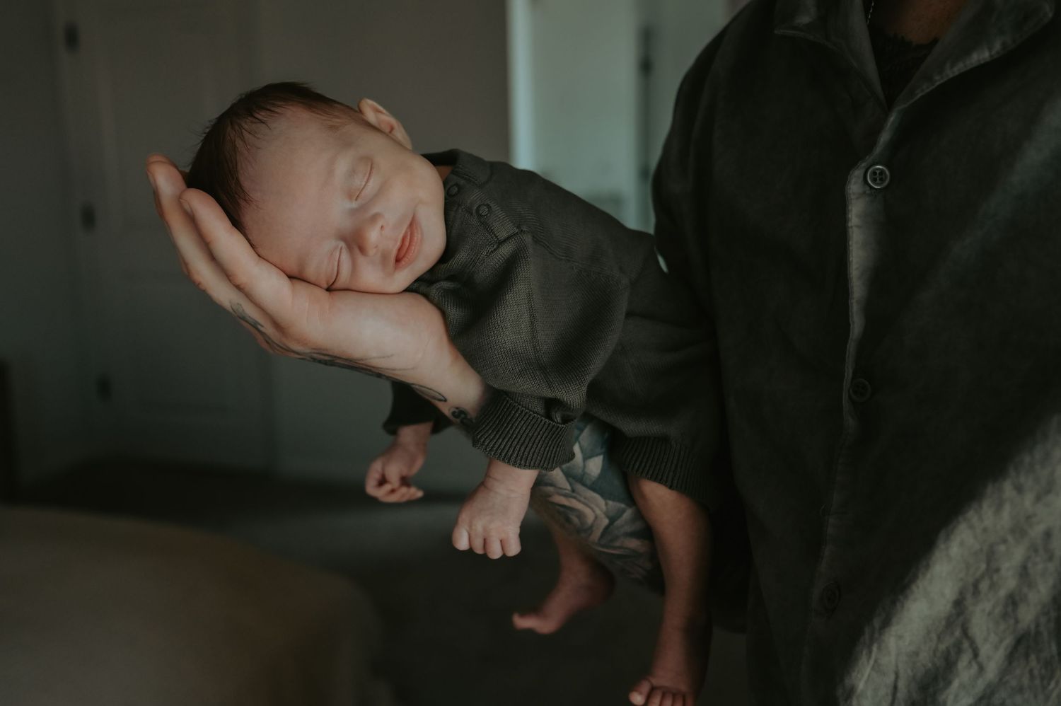 A peaceful newborn baby sleeping in an adult's hand, dressed in a gray outfit, captured in a tender moment.