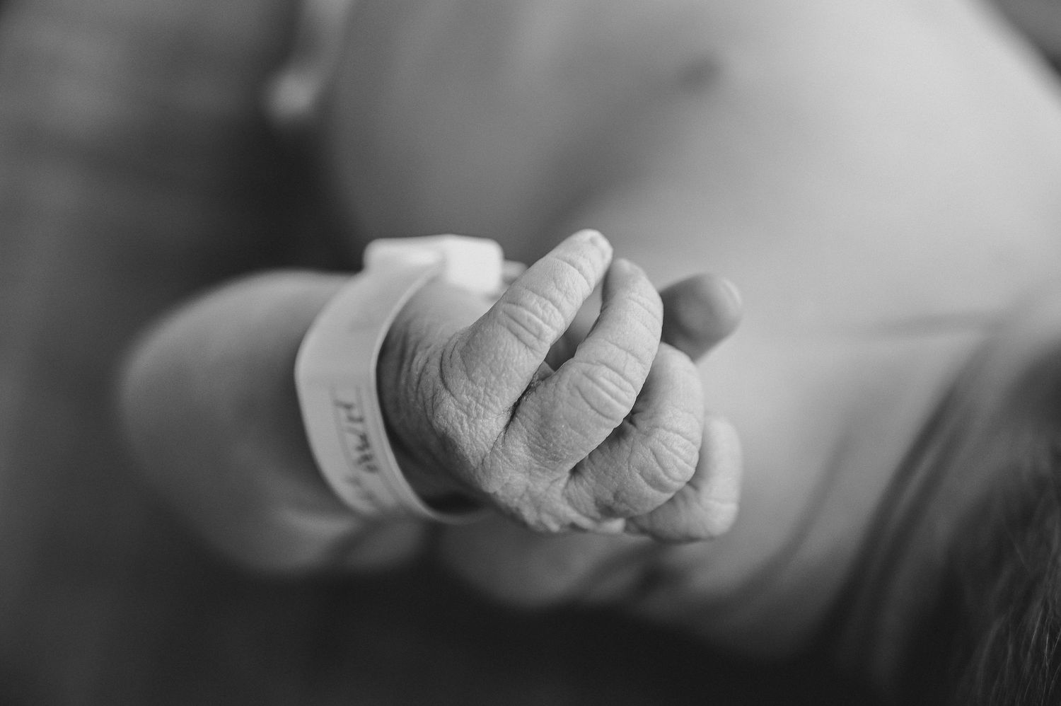Black and white close-up of a newborn baby's tiny hand with hospital ID bracelet.
