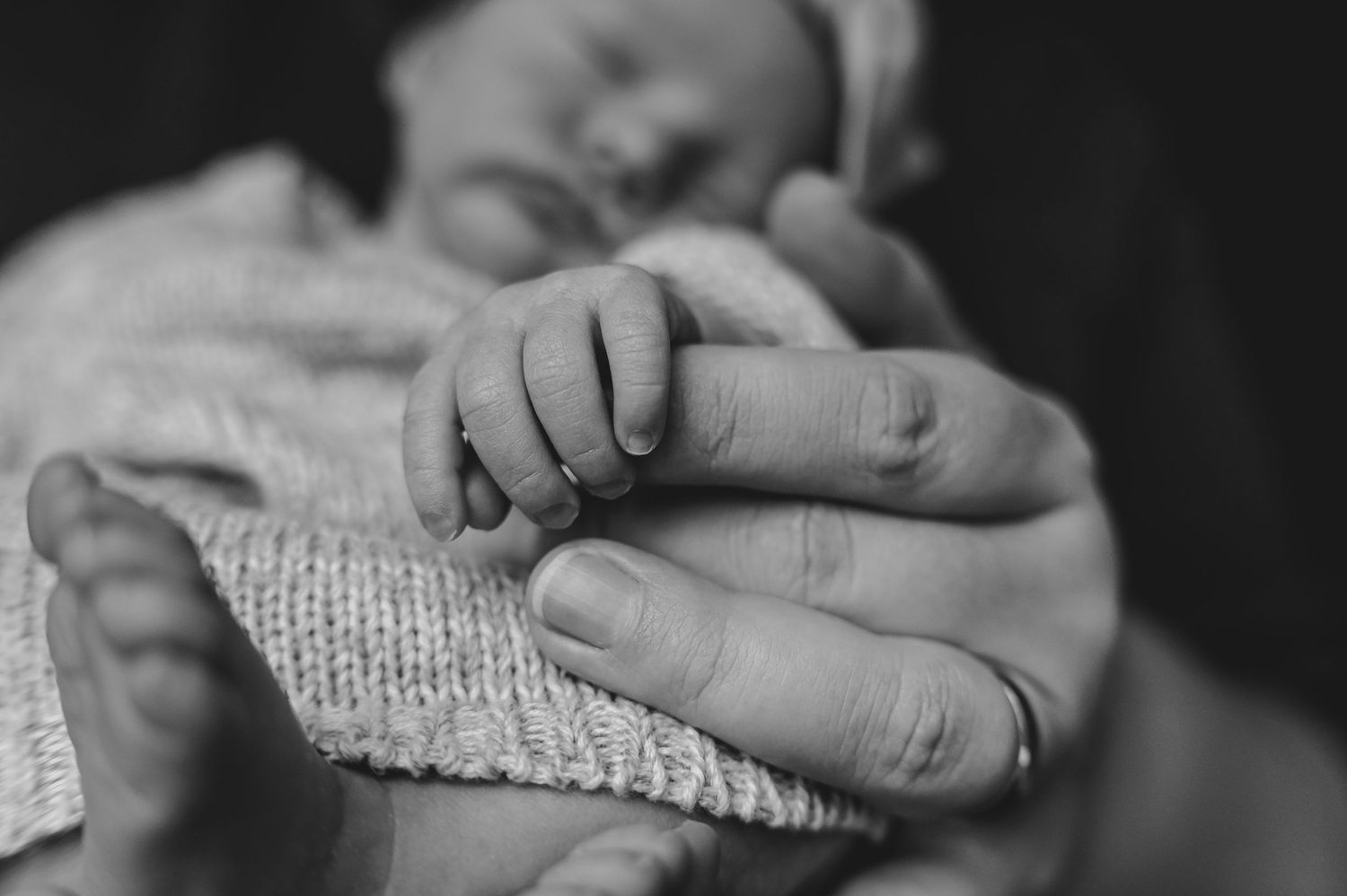 Black and white photo of a newborn baby's tiny hand grasping an adult's finger, symbolizing new life and parental love.