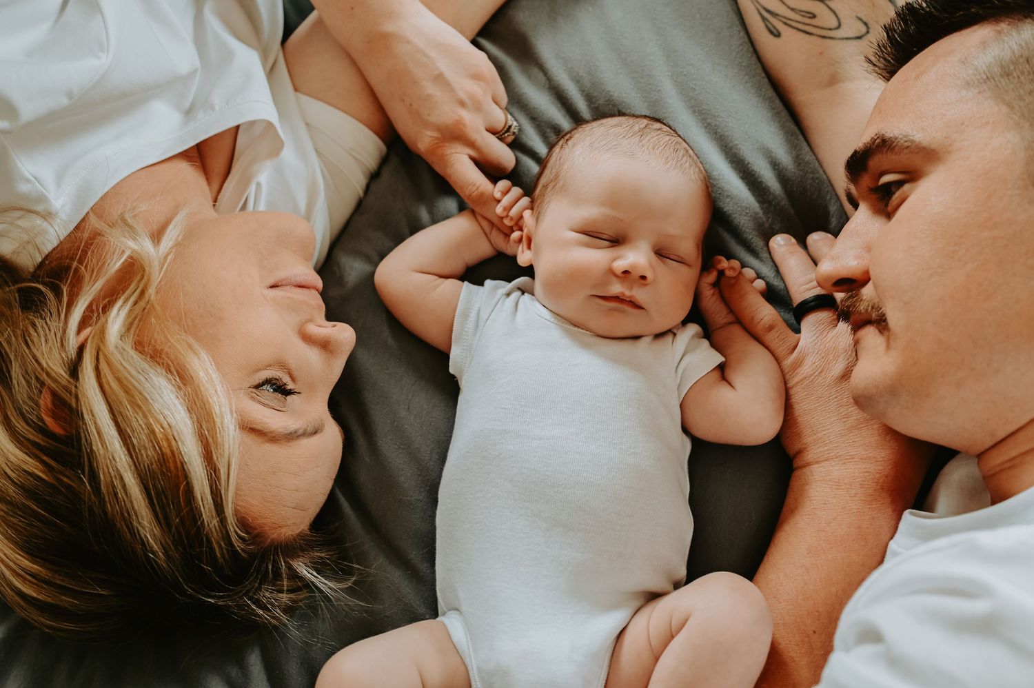 Happy parents lying beside their newborn baby, sharing a tender family moment together.