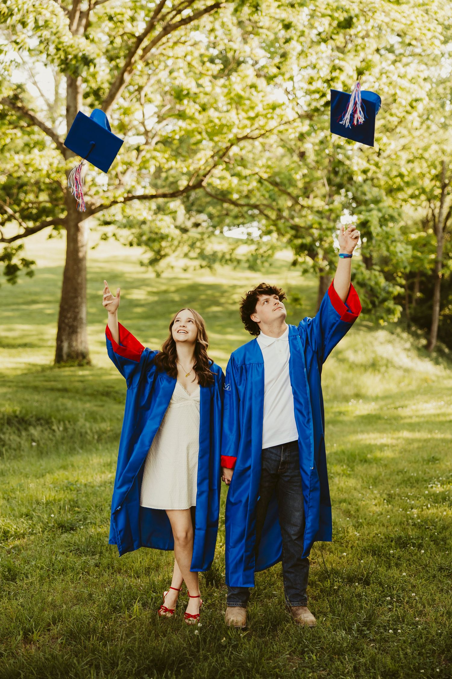Two graduates in blue gowns toss their caps in the air outdoors, celebrating their graduation milestone.