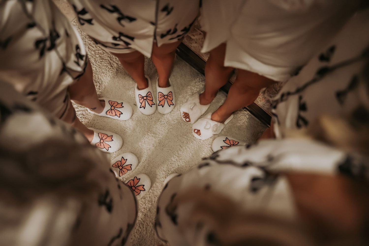 Circle of feet wearing matching white slippers shown from above on wooden floor.