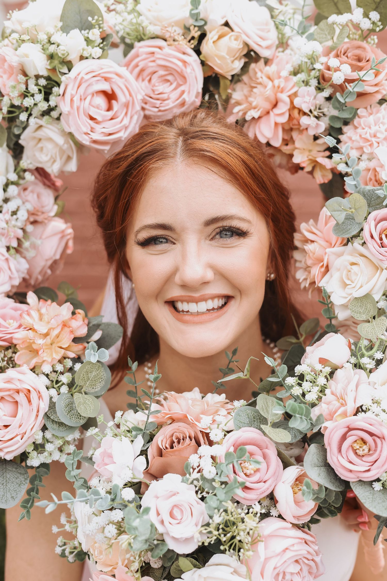 A bridal portrait framed by a stunning arrangement of pink roses and soft greenery.