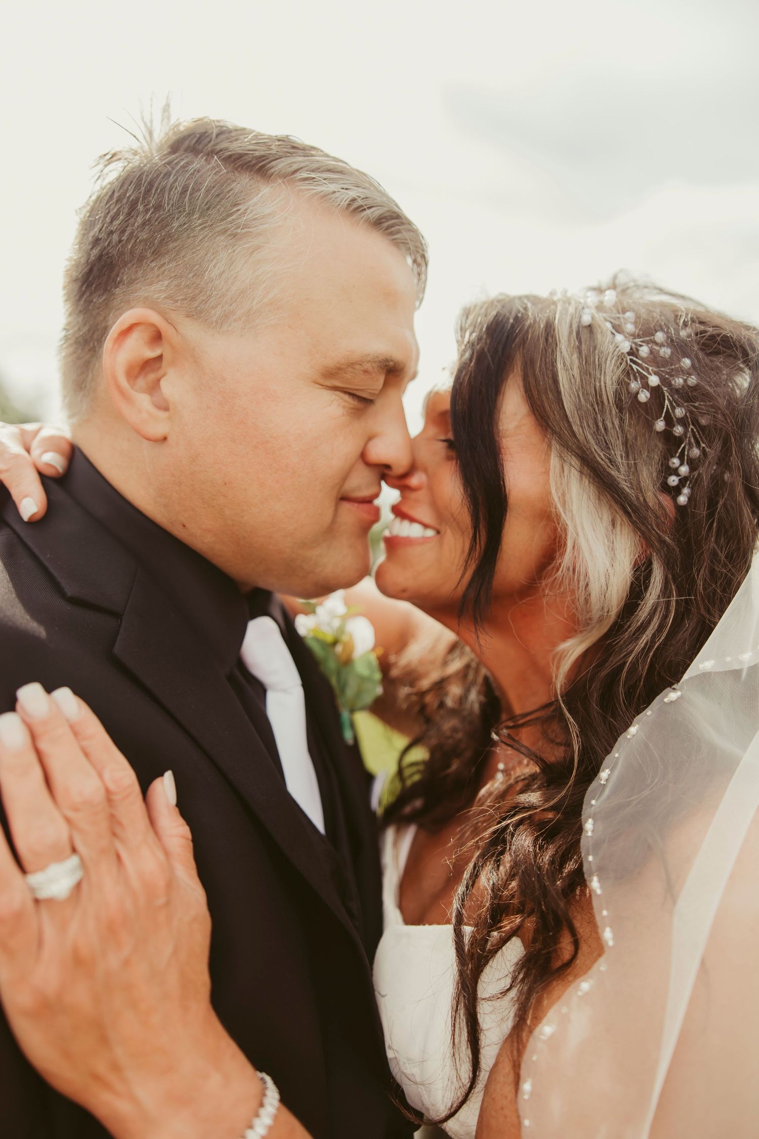 A bride and groom share a romantic almost-kiss moment, with the bride wearing a floral hair piece and veil on their wedding day.