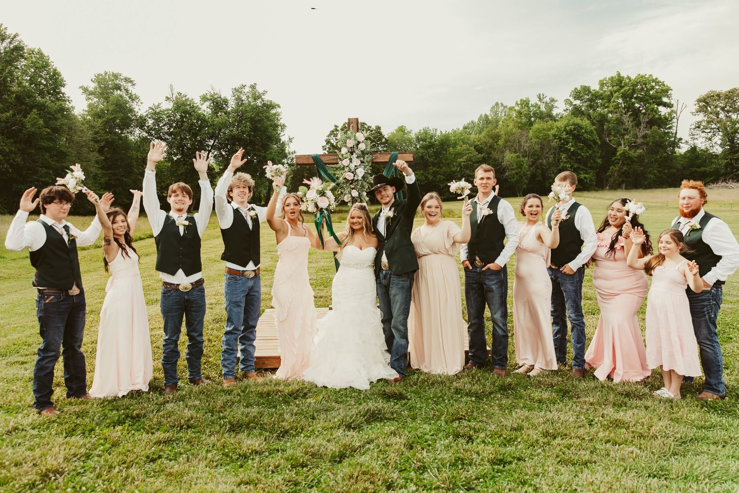 Wedding party celebrating outdoors on green lawn, bride and groom with bridal party in blush pink dresses and navy vests.