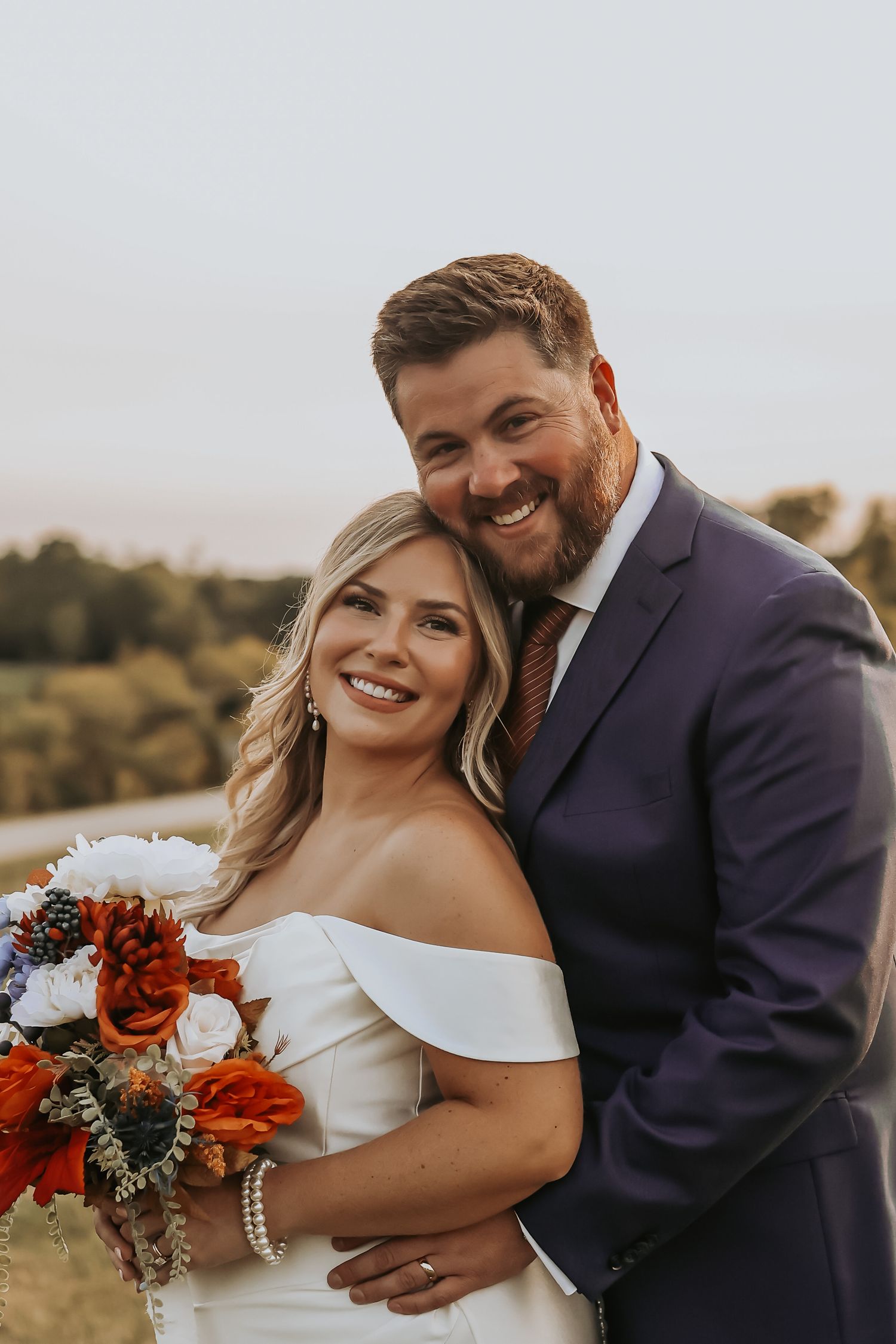 Joyful wedding portrait shows happy couple smiling together with autumn landscape backdrop.