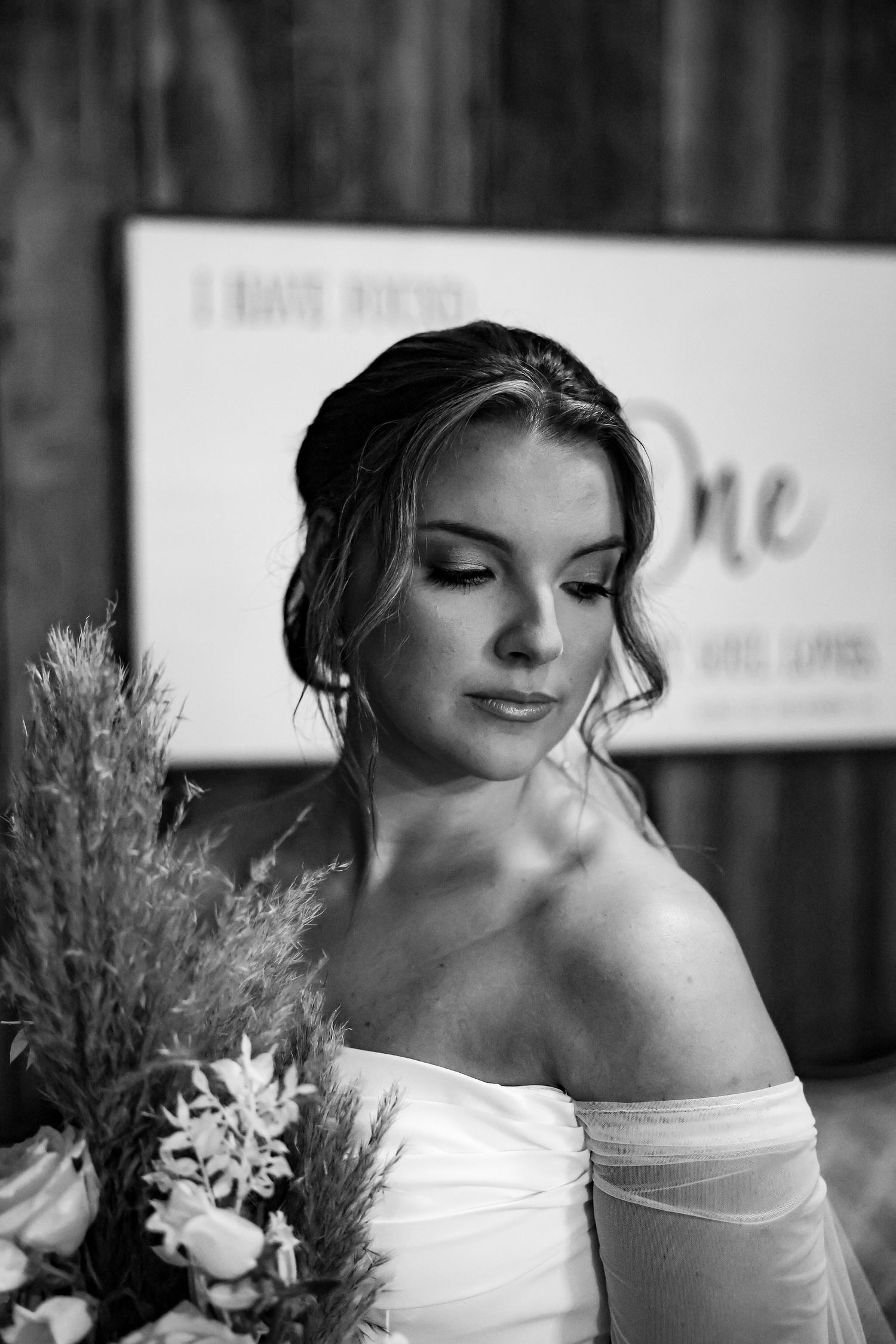 A serene bridal portrait in black and white showcasing elegant off-shoulder gown with floral bouquet.
