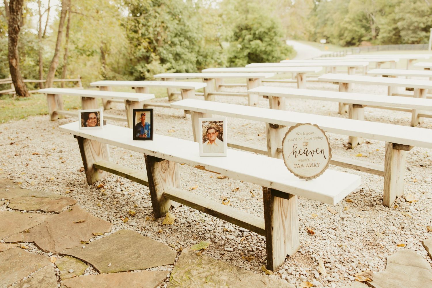 Outdoor wedding ceremony benches with memorial photos and a heaven sign honoring loved ones, set in a wooded venue.