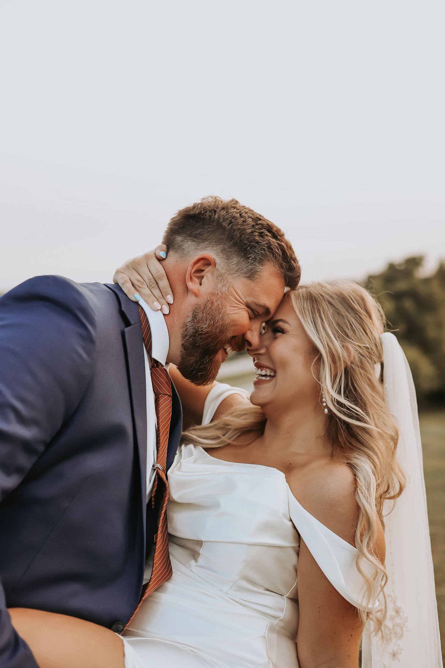 Intimate moment between newlyweds sharing a smile during outdoor wedding photoshoot.