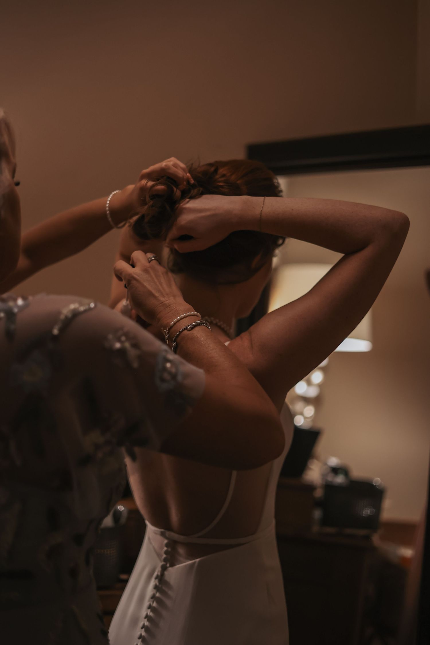 Behind-the-scenes wedding preparation showing dress details in warm lighting.