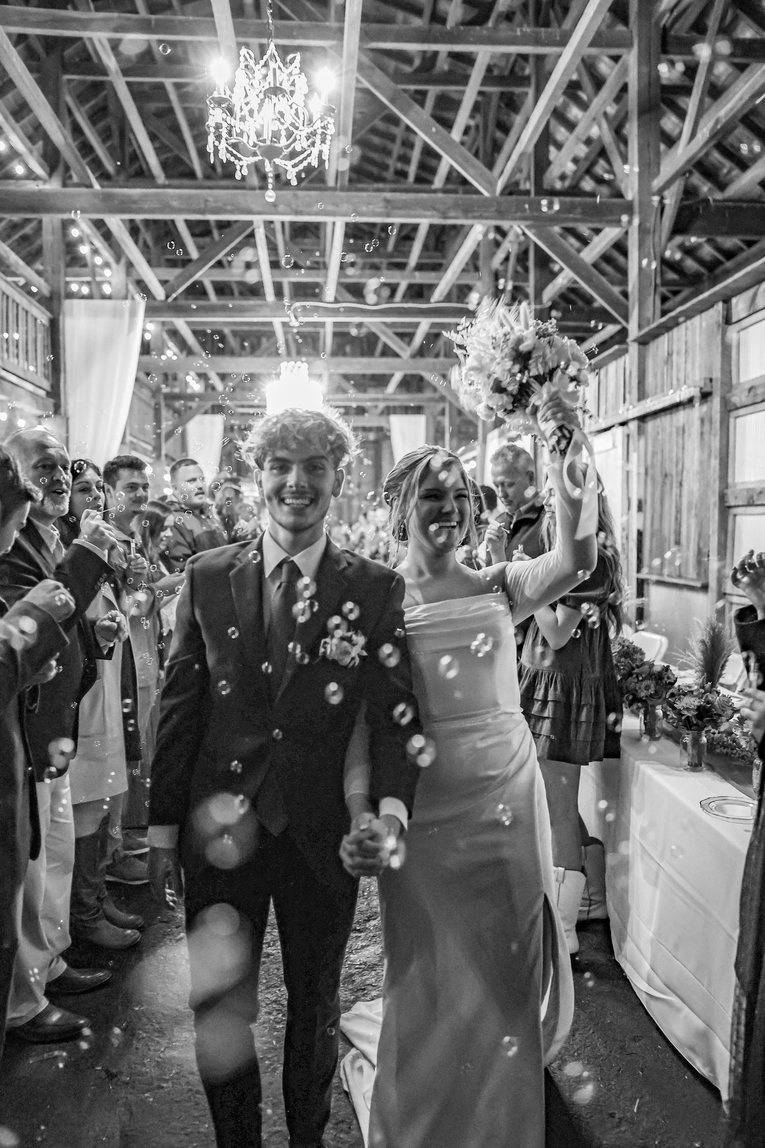 A black and white photo of newlyweds celebrating their exit while guests shower them with confetti.