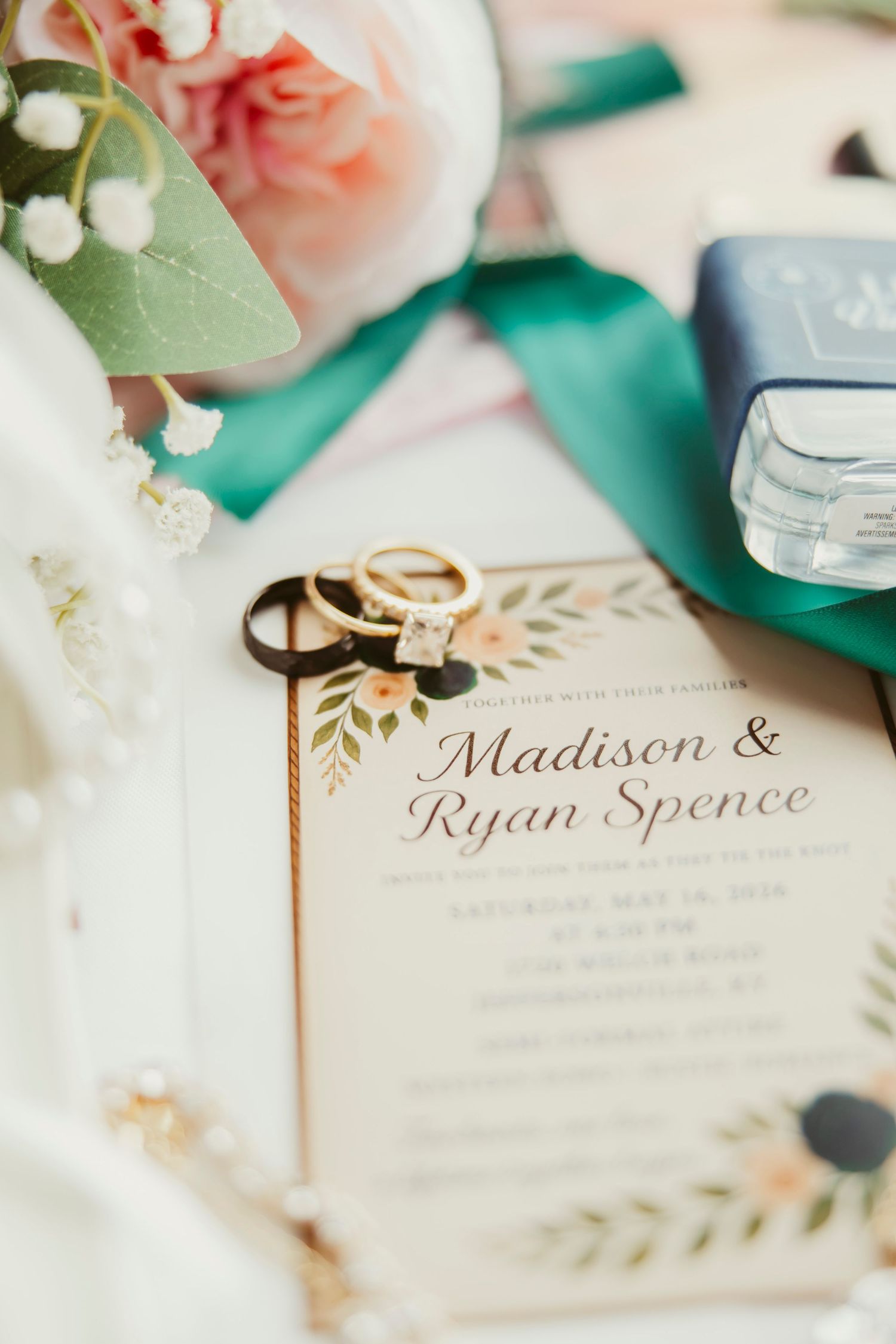 Wedding invitation for Madison & Ryan Spence with gold rings, pink roses, green ribbon, and floral details on a white background.