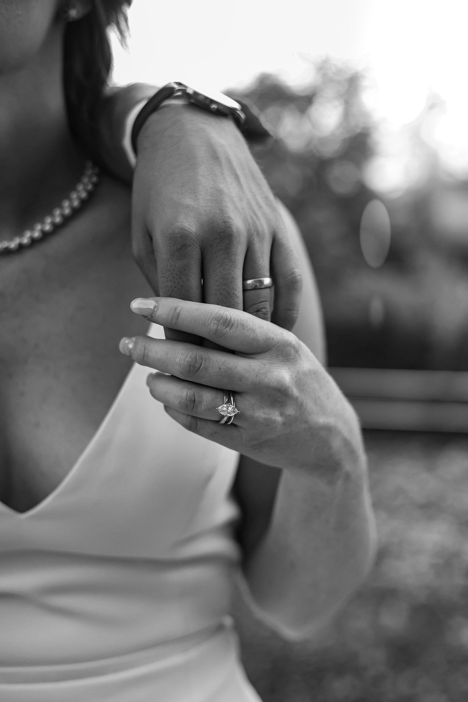 Close-up black and white photo of hands showing wedding rings and engagement ring.