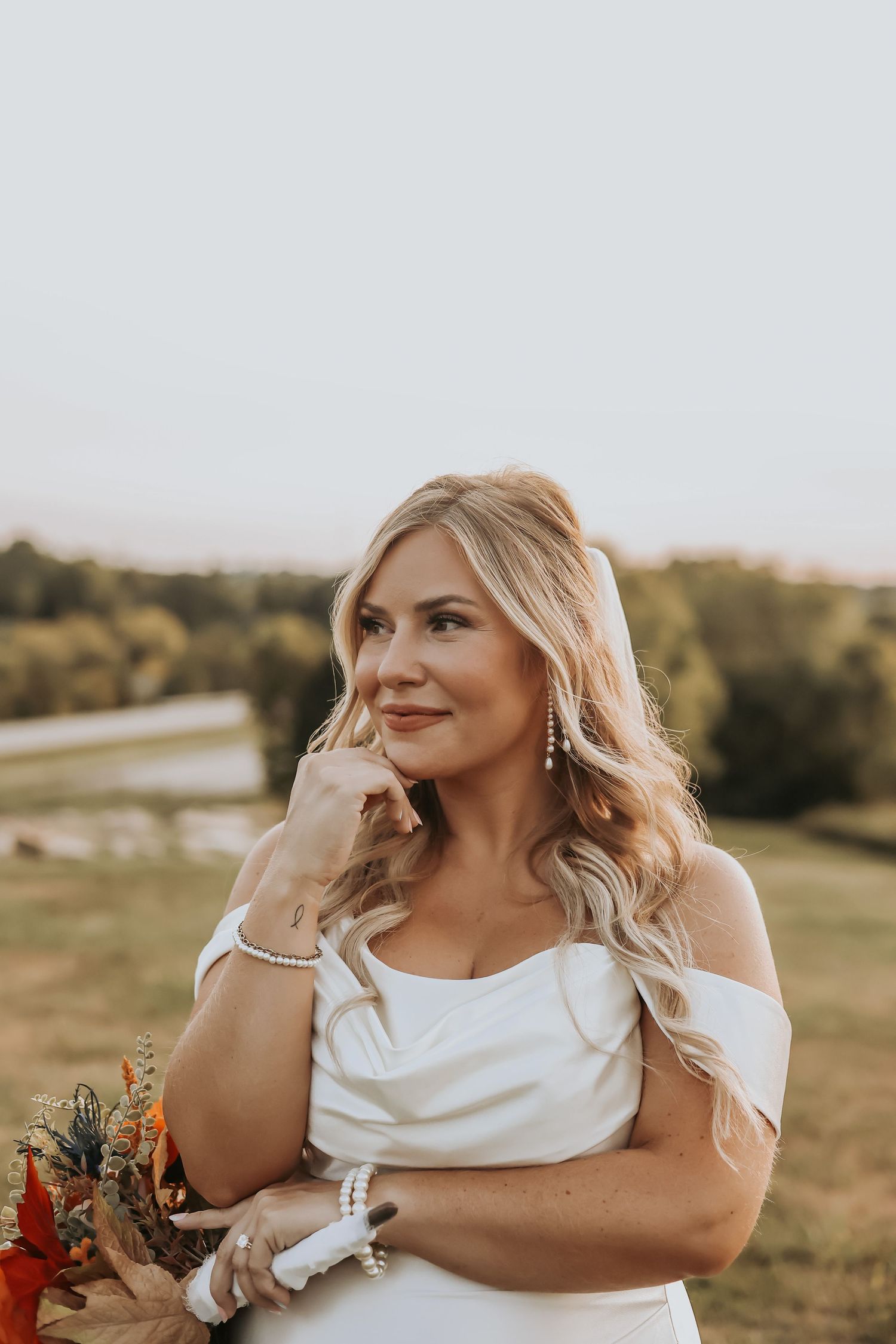 Bride with elegant jewelry poses against natural outdoor backdrop.