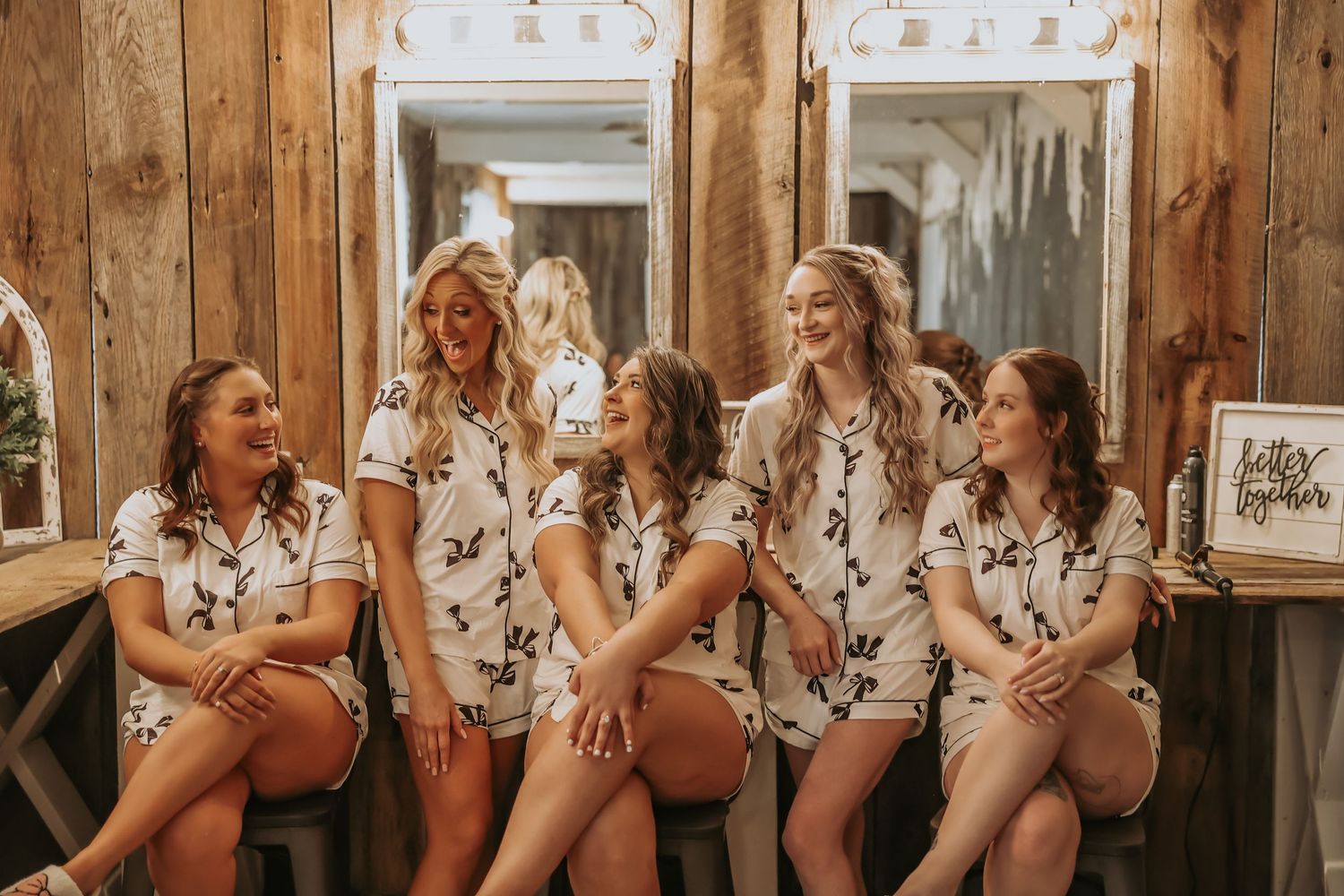 Friends in coordinated floral loungewear share laughs while sitting on wooden bench.