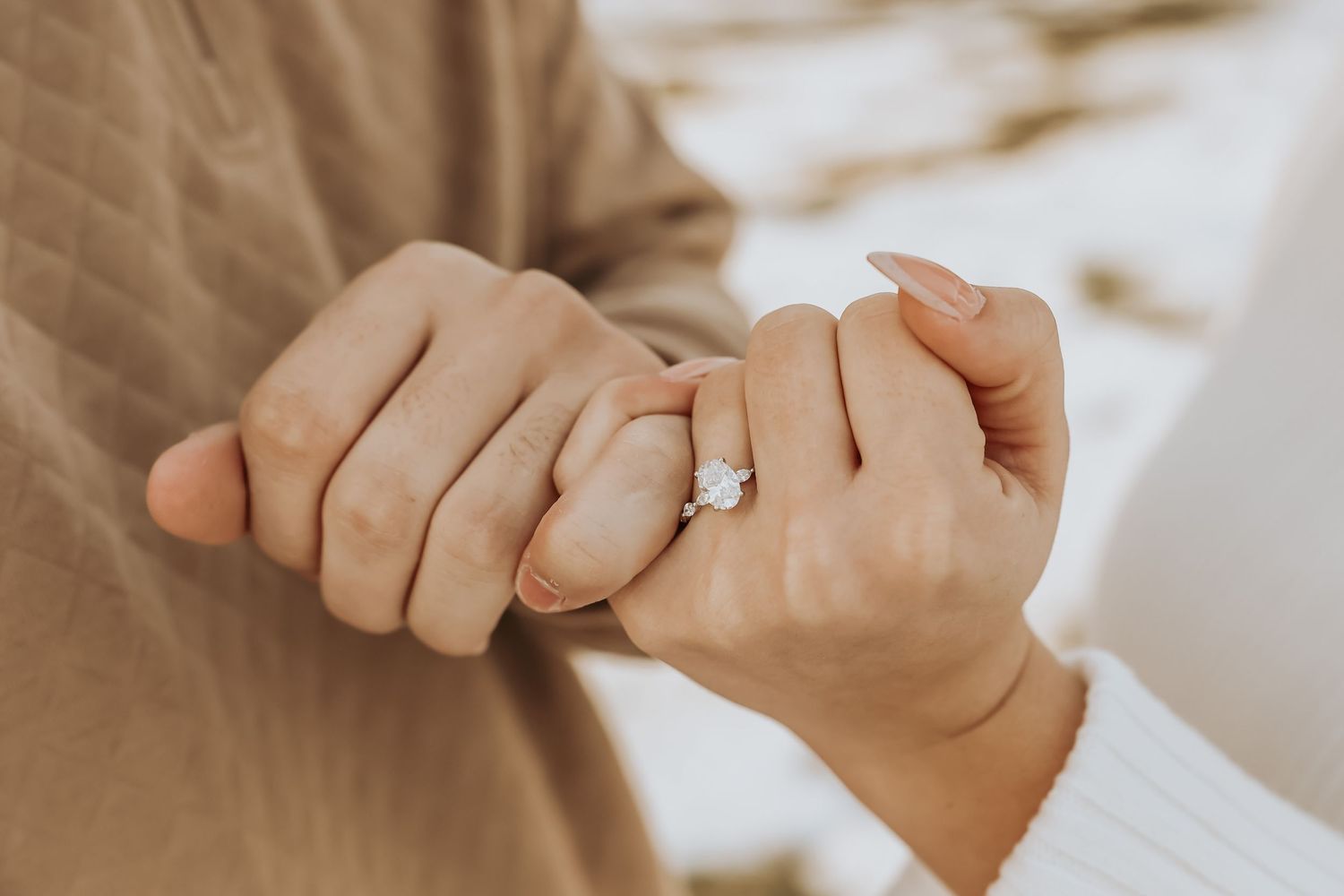 Close up view of interlocked hands with an engagement ring glowing in soft natural light.