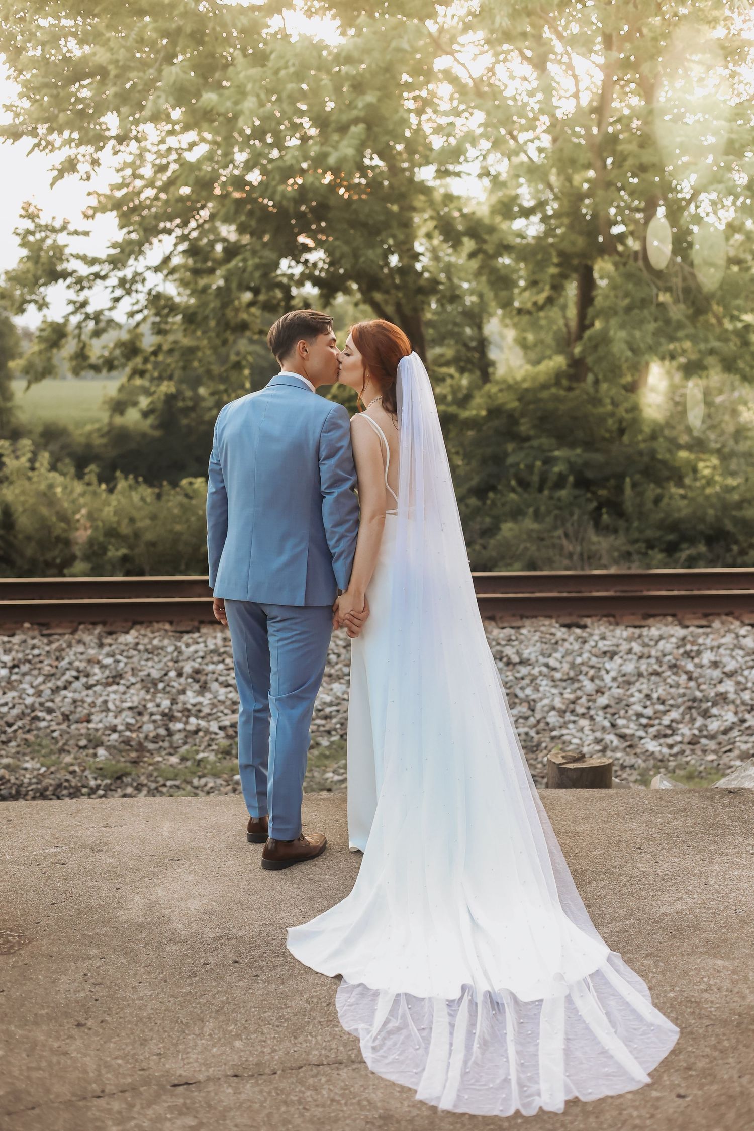 A romantic wedding portrait of newlyweds sharing a moment on railroad tracks at golden hour.