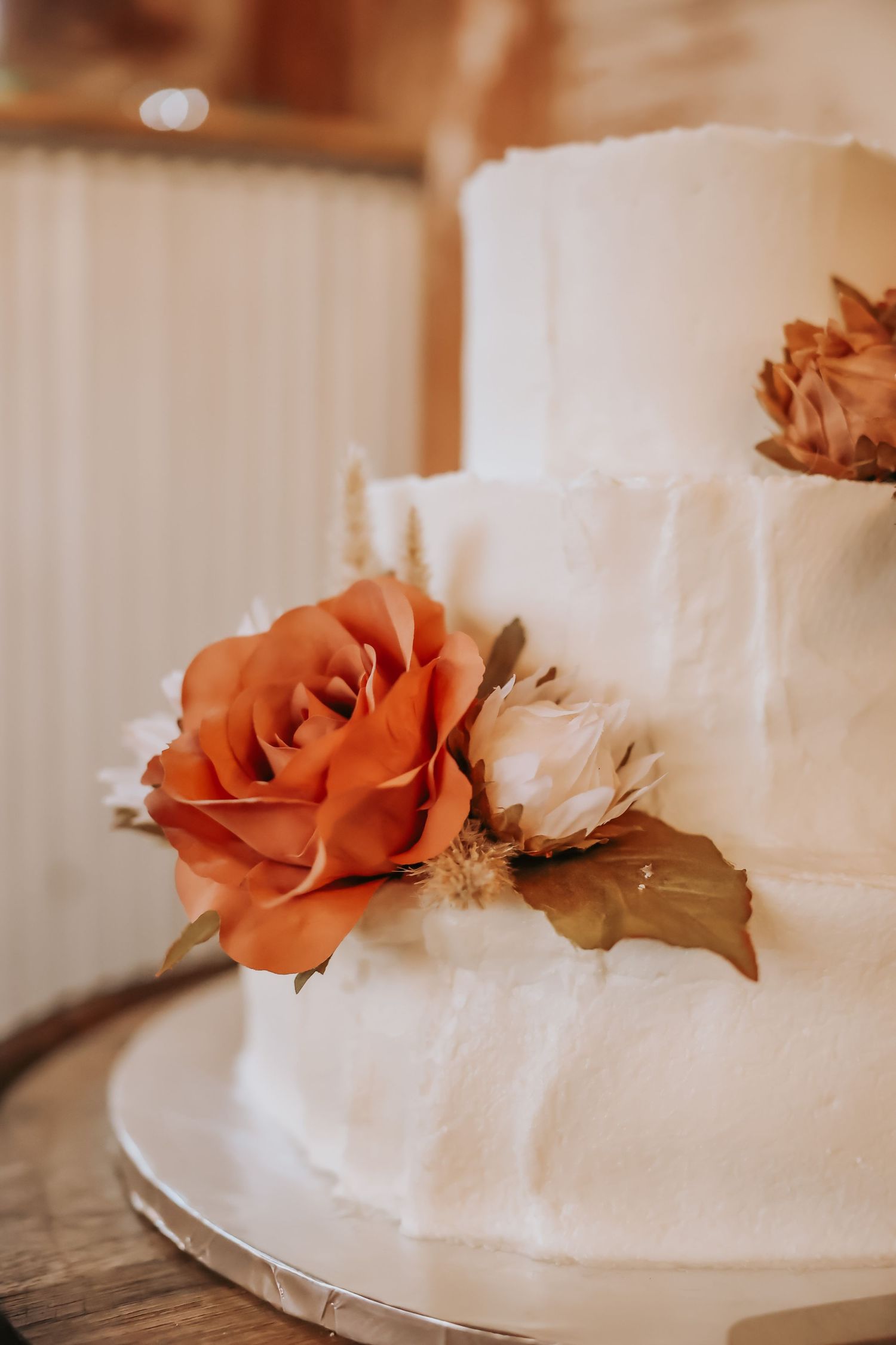Elegant white wedding cake decorated with burnt orange and cream roses.