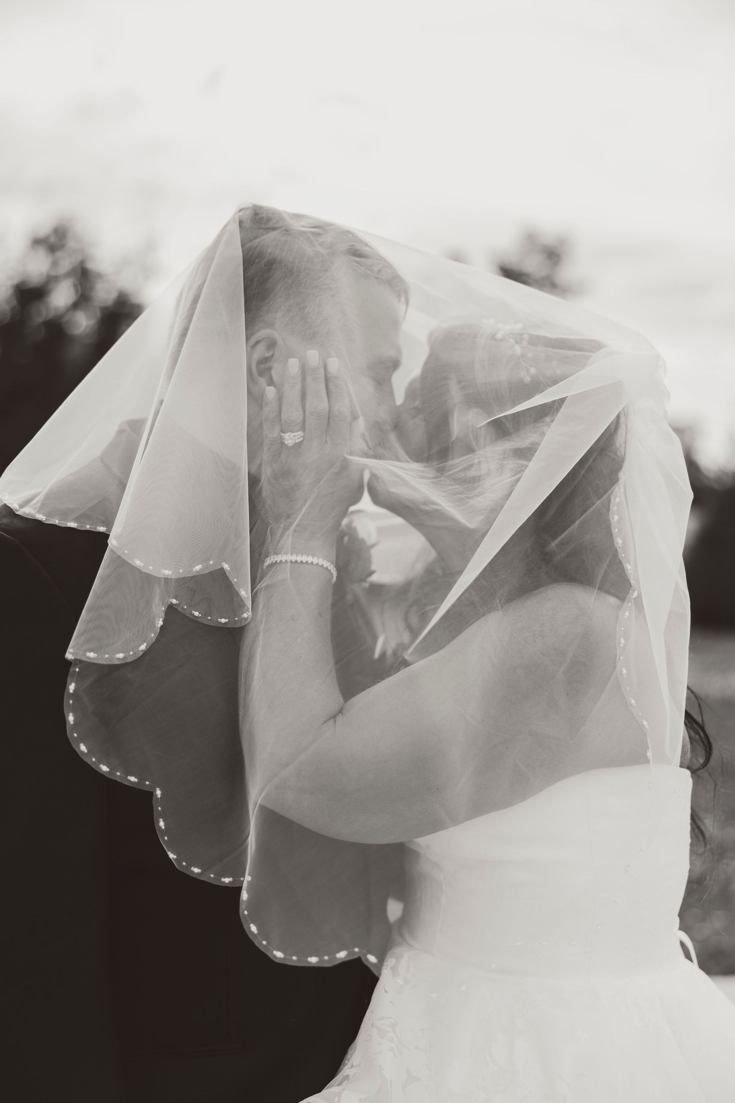 Black and white photo of bride and groom sharing a kiss hidden beneath the brides flowing wedding veil.