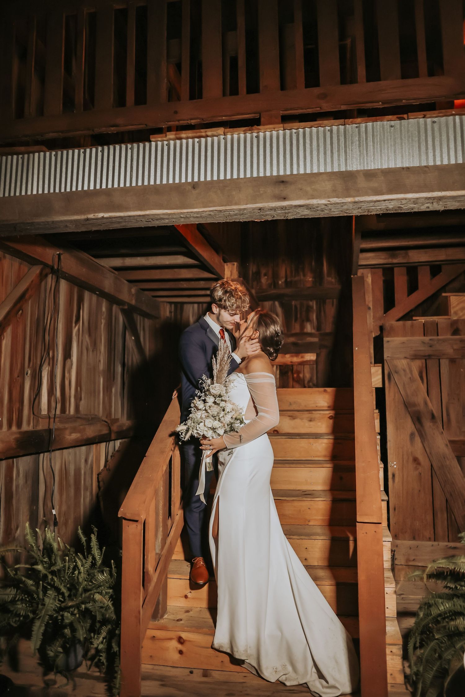 A romantic wedding portrait in a rustic wooden barn staircase with natural lighting.