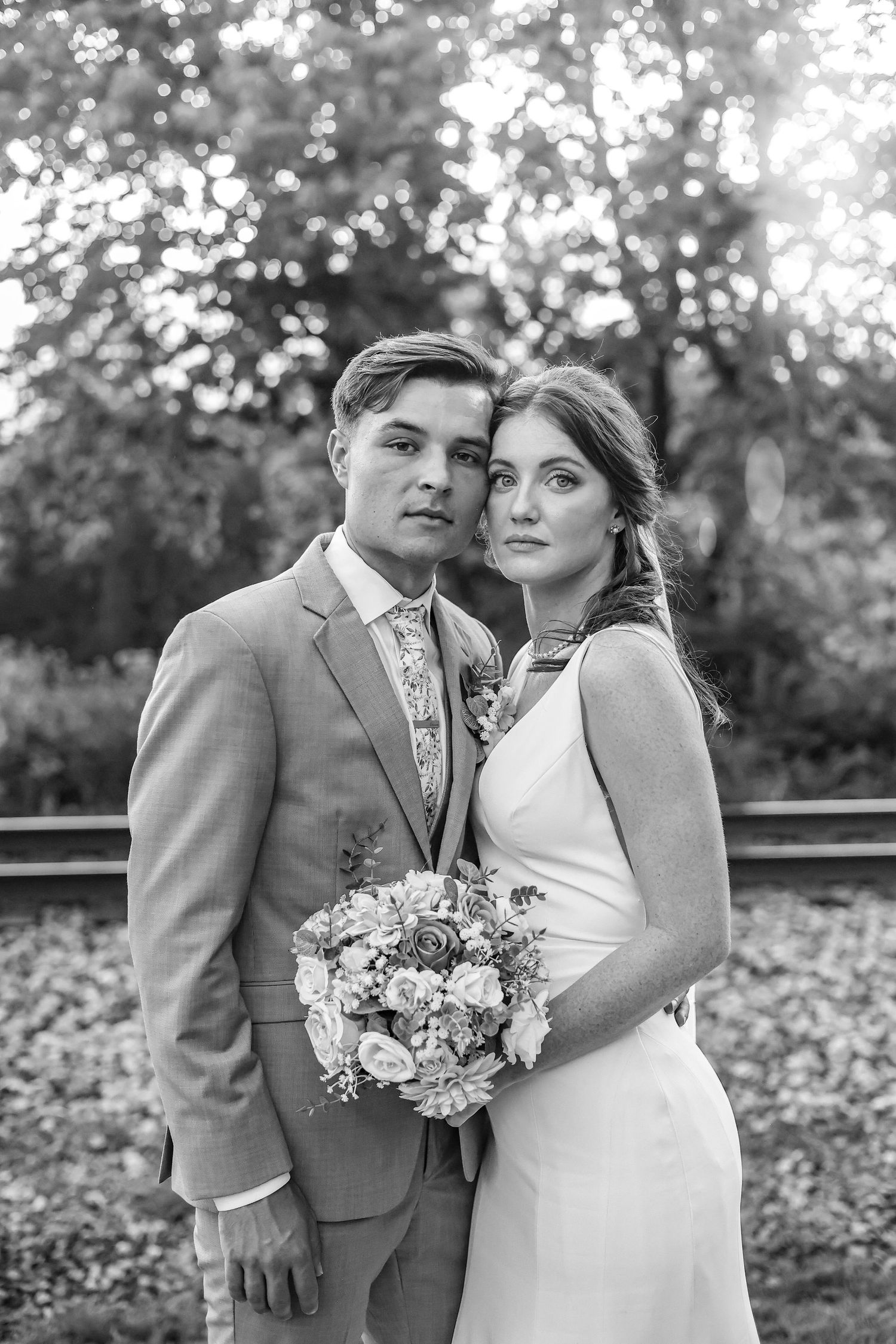 Black and white wedding portrait of a couple posing outdoors with a floral bouquet.
