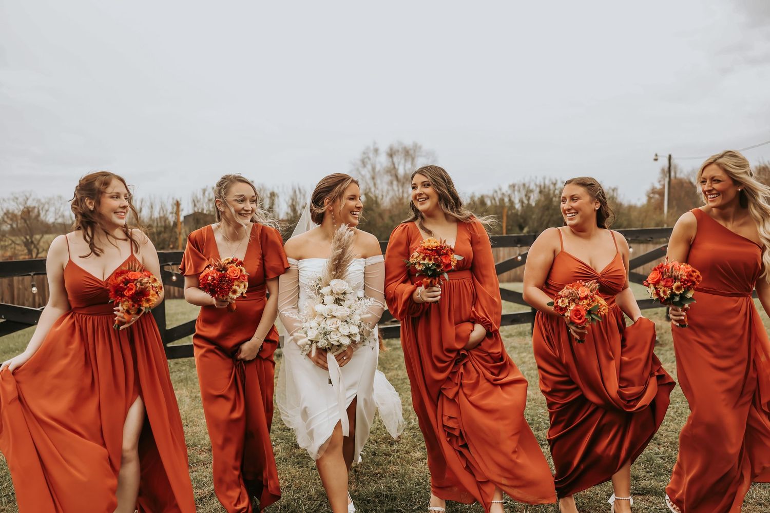 Wedding party in flowing red dresses walks and laughs together outdoors.