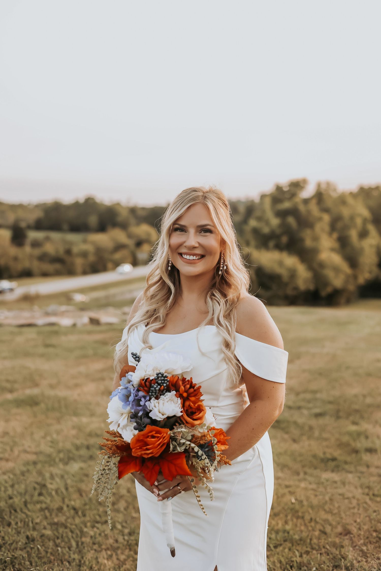 Bride poses with colorful autumn bouquet in an off-shoulder wedding gown outdoors.
