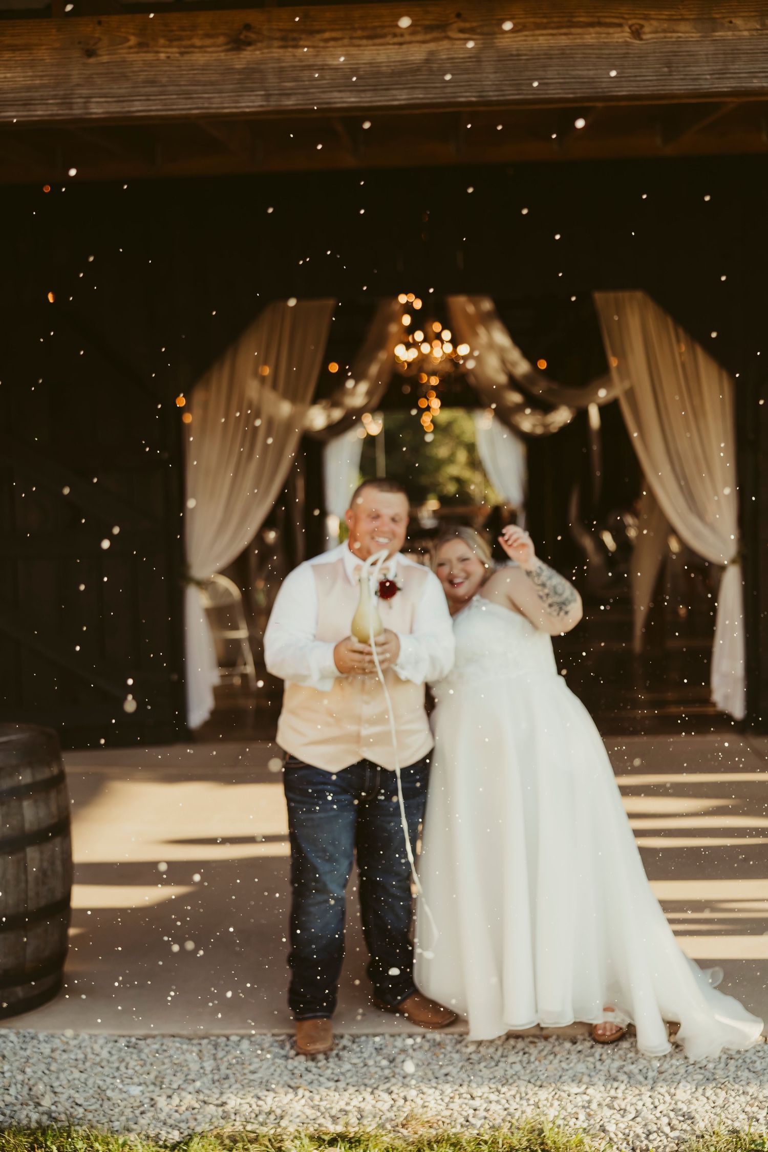 Newlyweds celebrate with sparklers outside decorated barn venue with confetti falling.