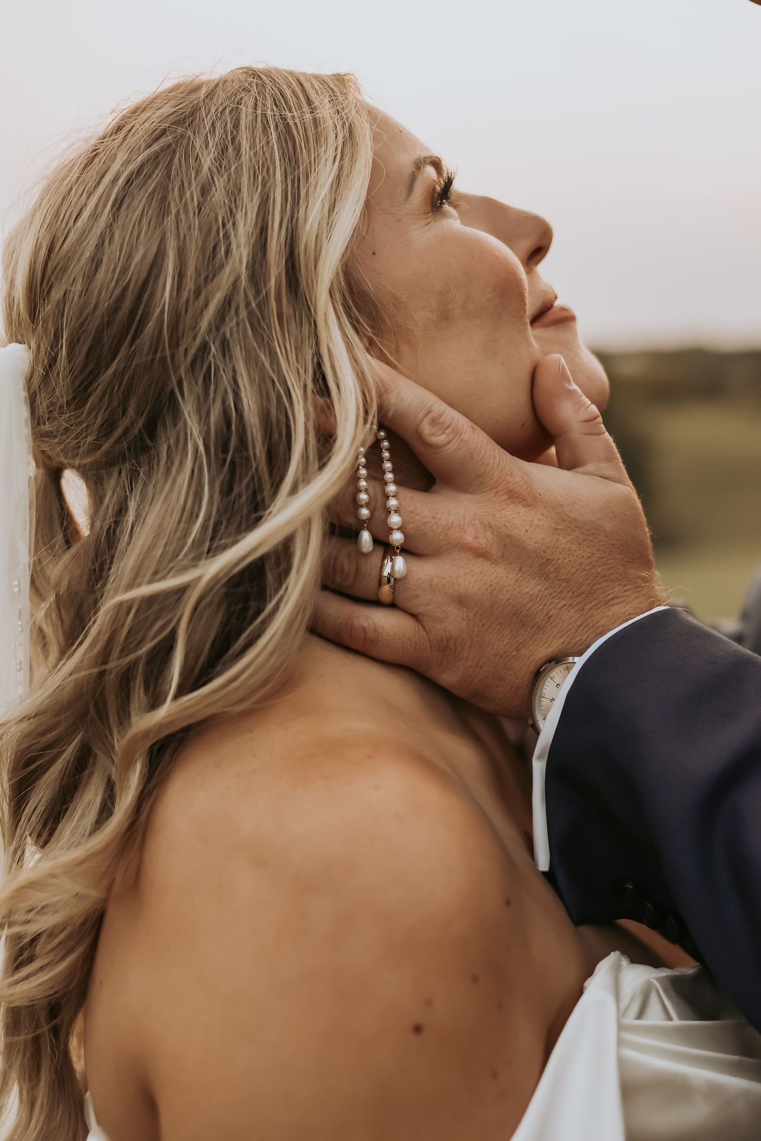 A tender romantic moment between newlyweds as hands caress against the backdrop of an outdoor setting.
