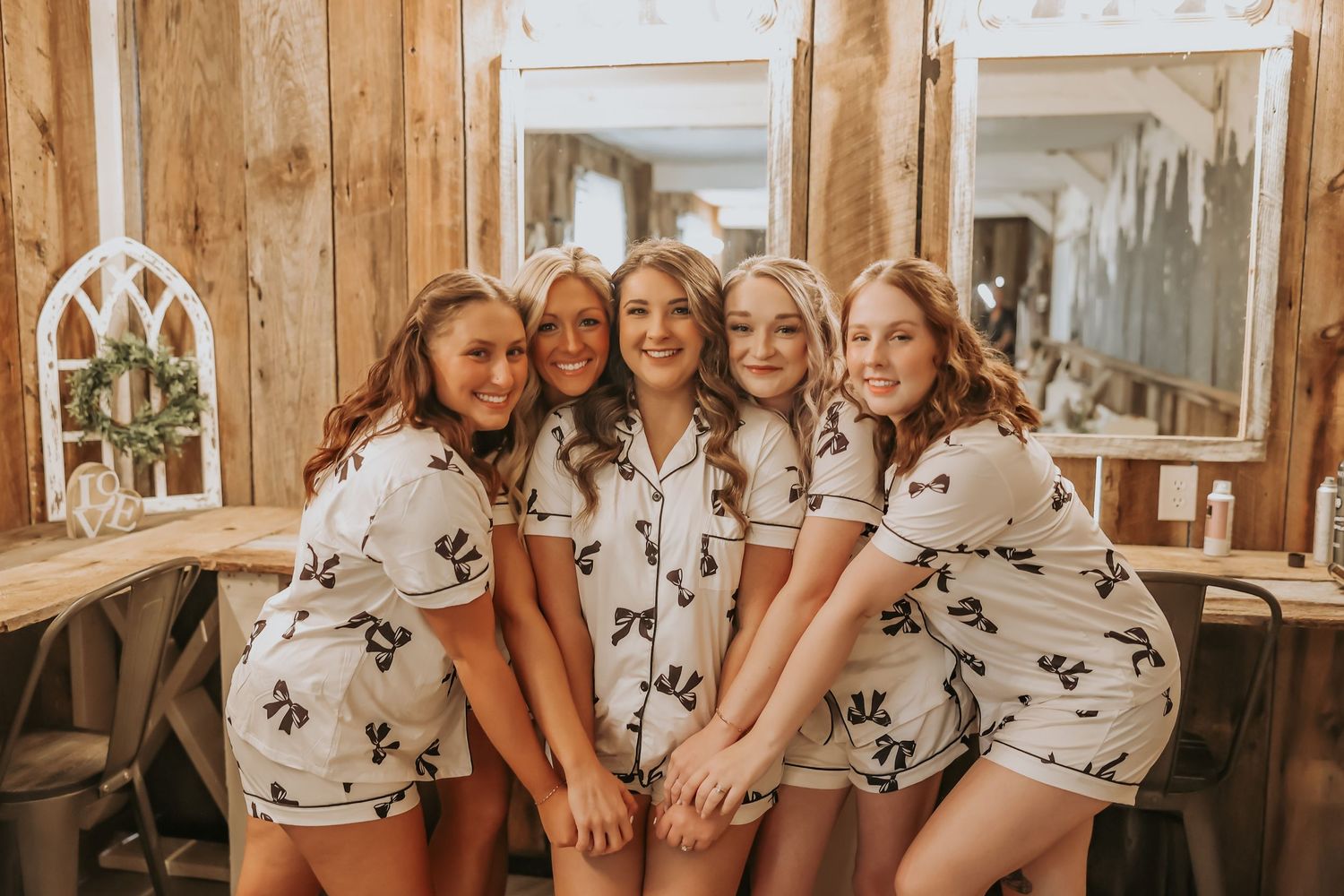 Group wearing matching floral pajama sets pose playfully in rustic wooden room with mirrors.