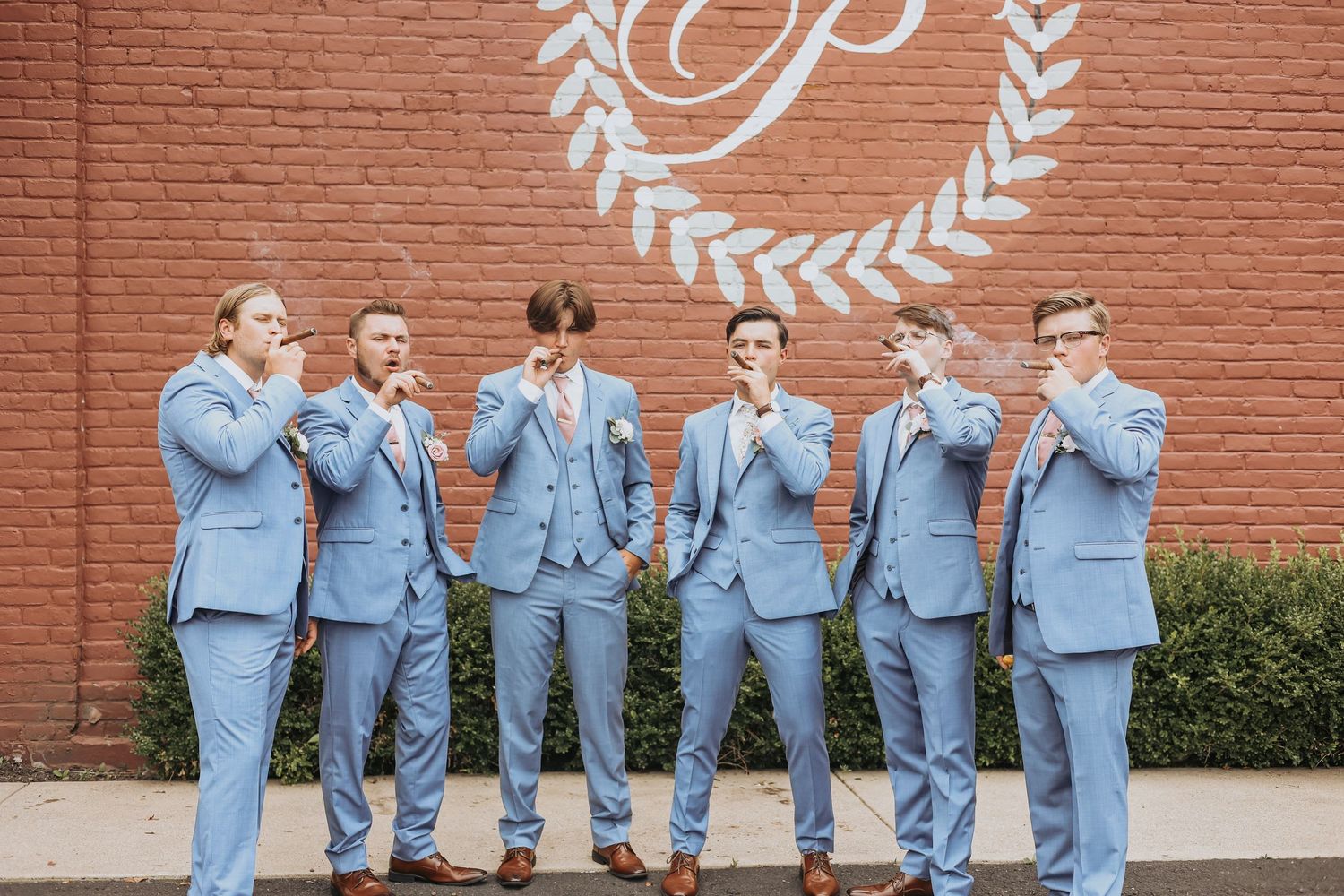 Wedding party in matching blue suits making funny faces against a brick wall.