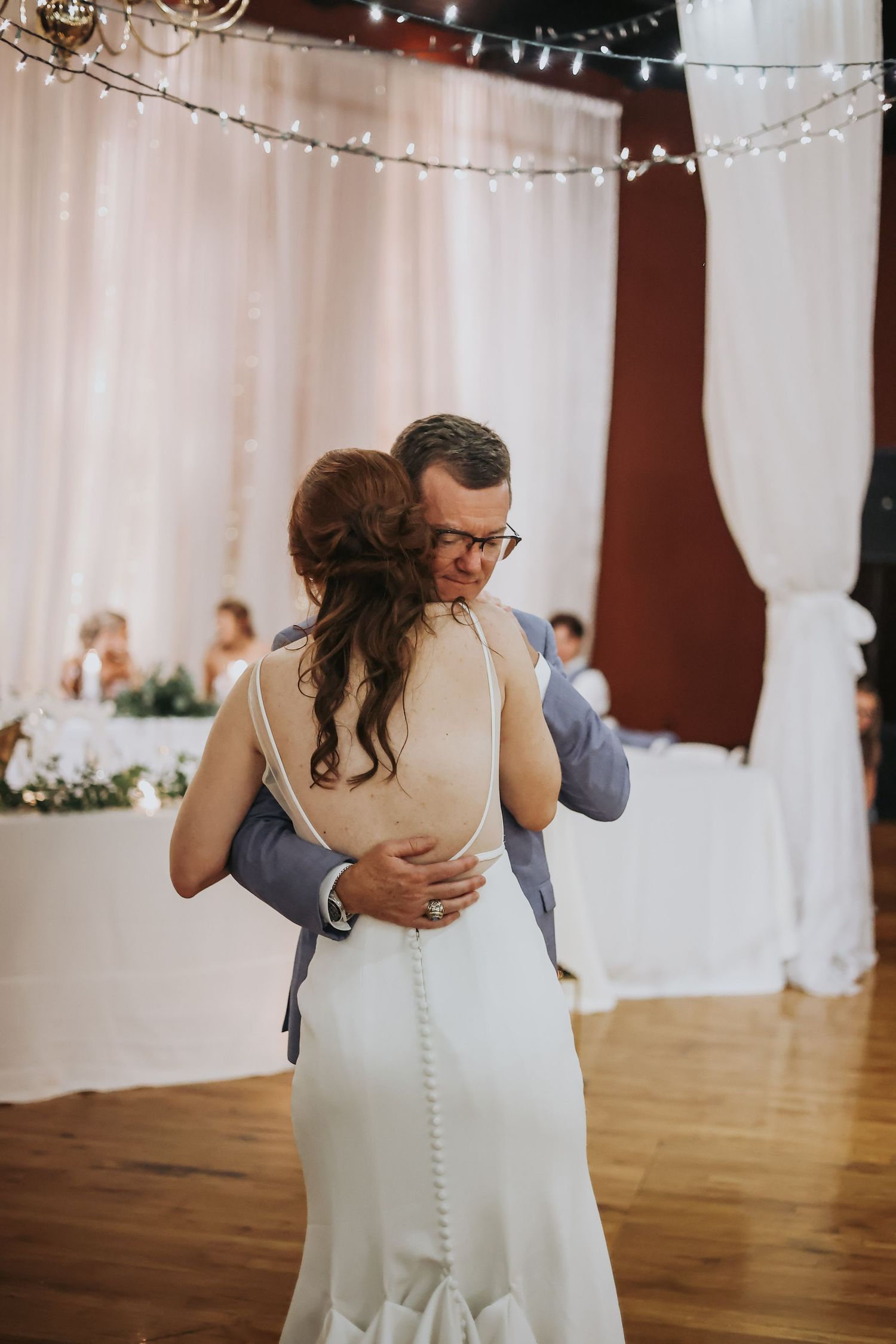 Couple sharing their first dance in an elegantly decorated reception venue with string lights.