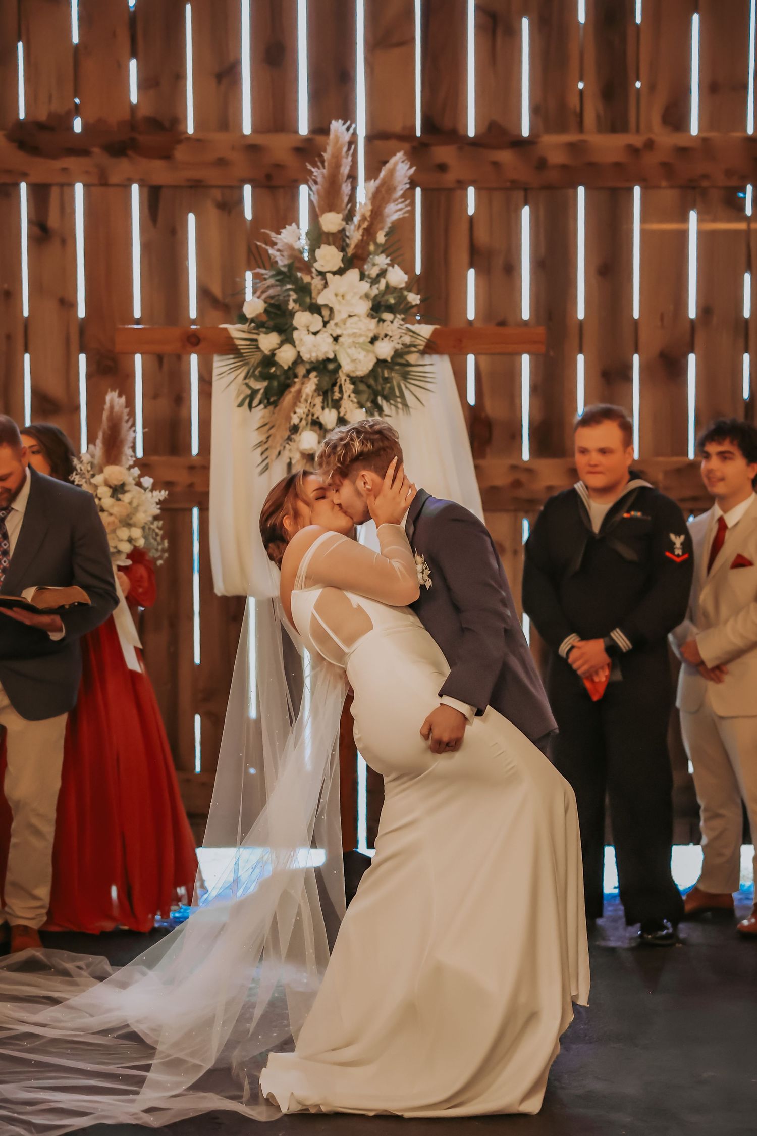 A wedding ceremony in a rustic barn setting with elegant floral arrangements and guests watching.