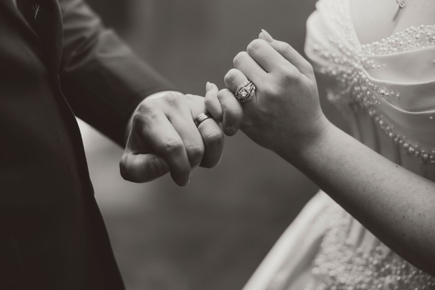 Black and white photo of a bride and groom holding hands, showcasing a diamond engagement ring at their wedding.