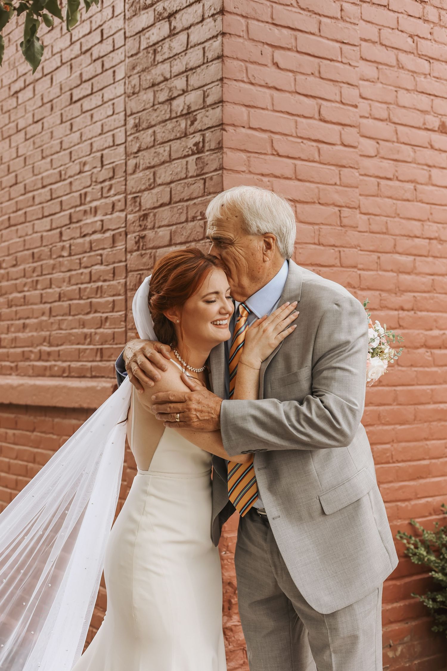 Emotional moment between bride and older gentleman against brick wall background.