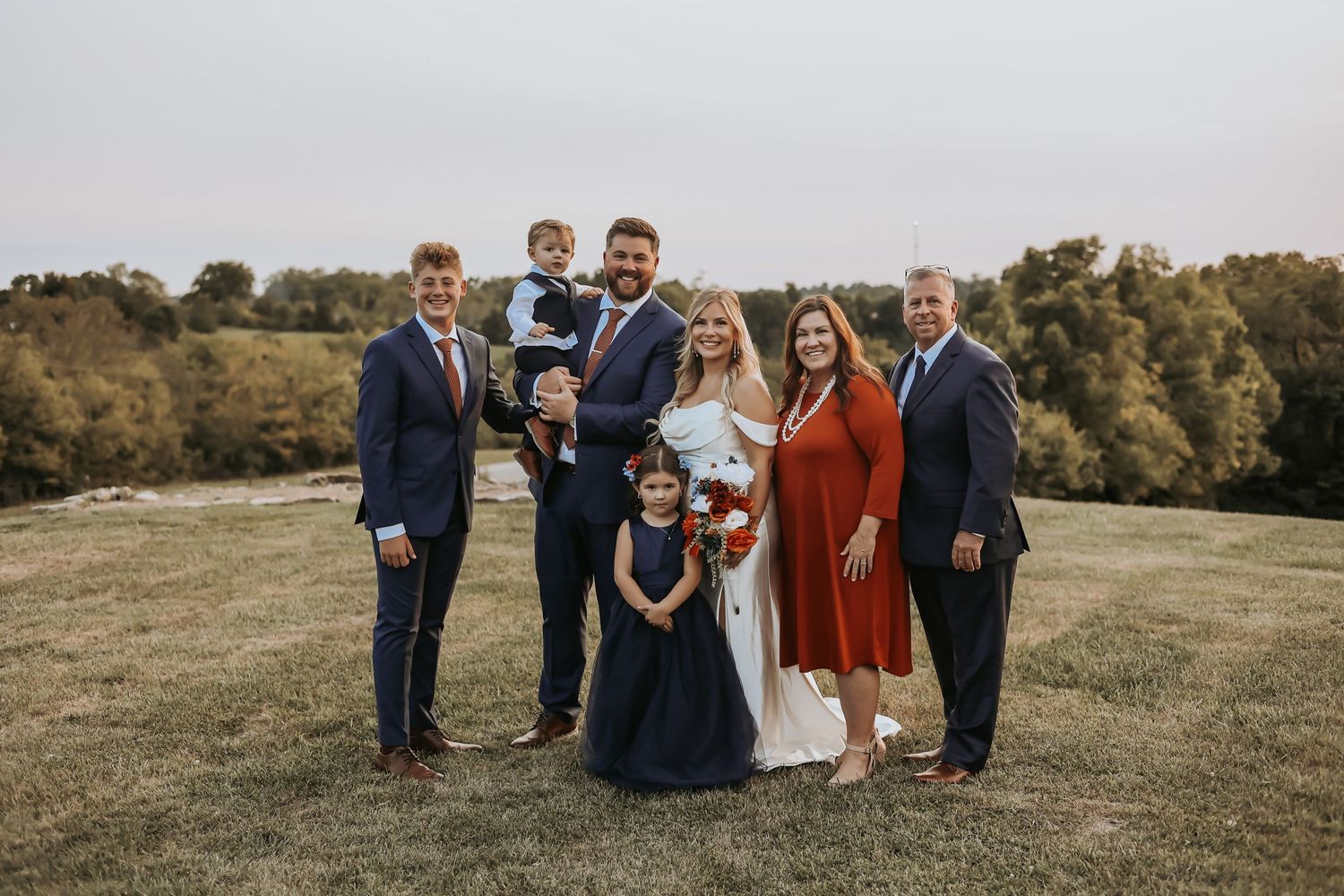 Wedding party group photo on a scenic hilltop with family members dressed in formal attire.